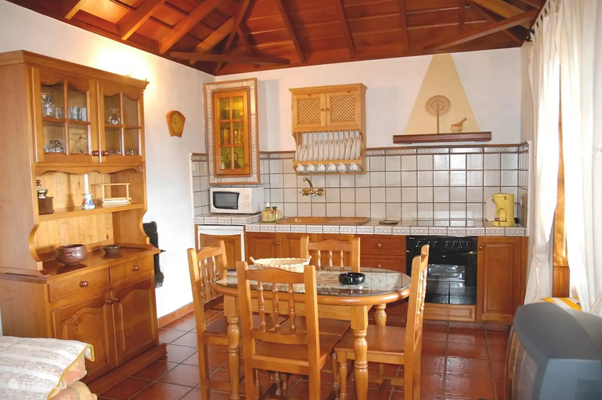 Keuken en eetkamer met keramisch fornuis, oven, magnetron, voorraadkast en servies.