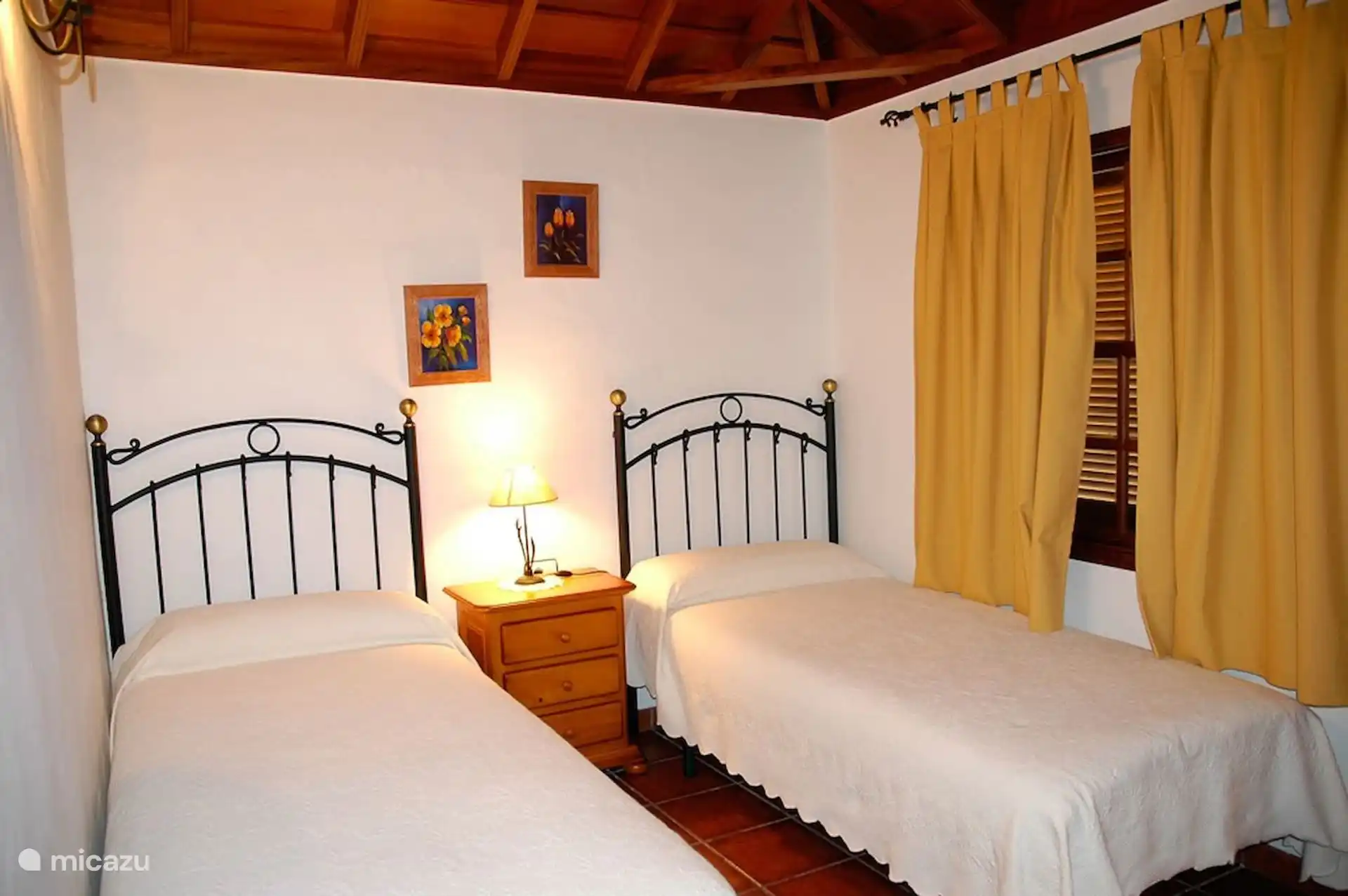 Slaapkamer met twee eenpersoonsbedden, smeedijzeren hoofdborden en een houten plafond.
