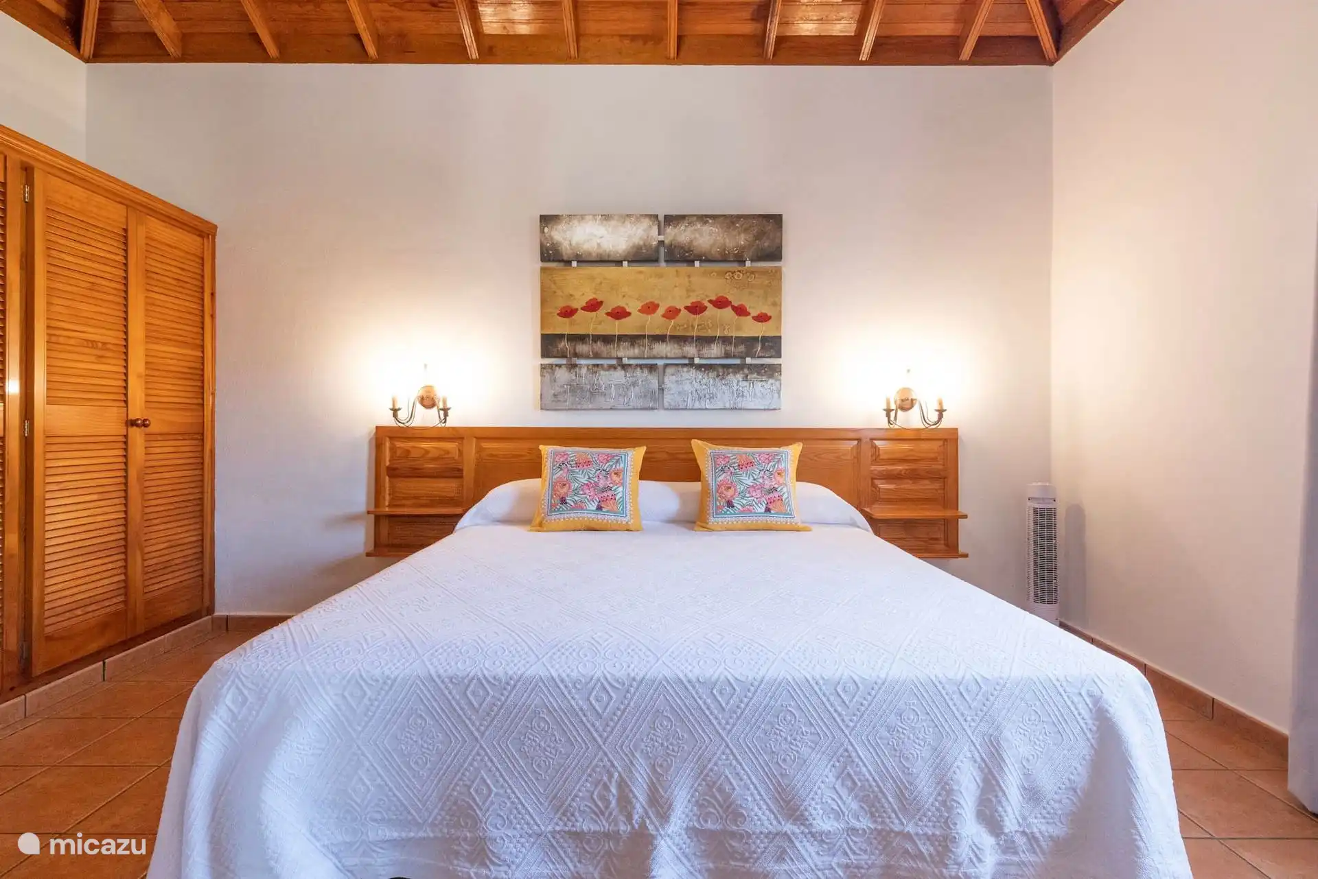 Slaapkamer met tweepersoonsbed, houten hoofdeinde met geïntegreerde nachtkastjes en kast met lattendeuren.