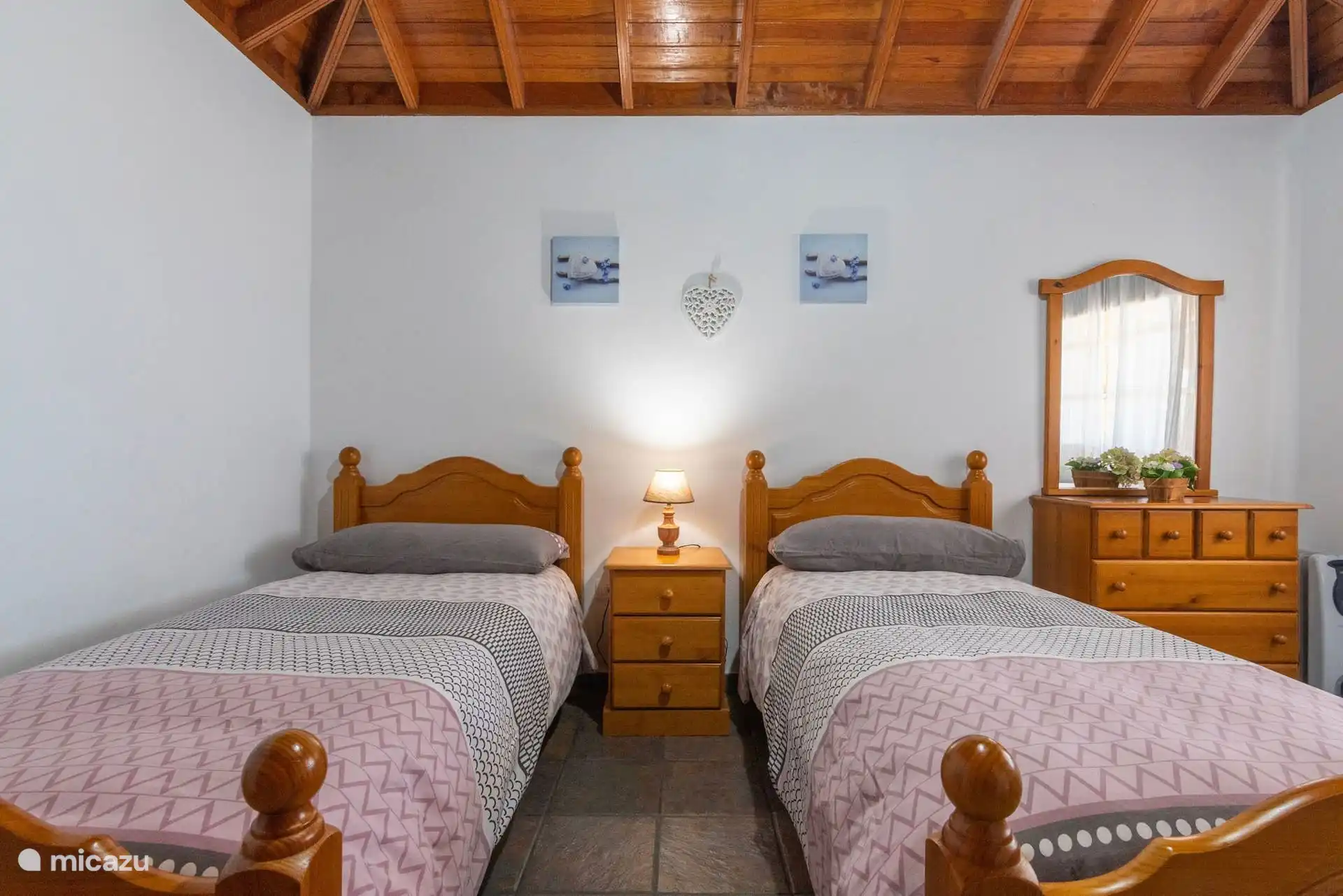 Chambre avec deux lits simples séparés par une table de chevet ; à droite, la commode avec un miroir.