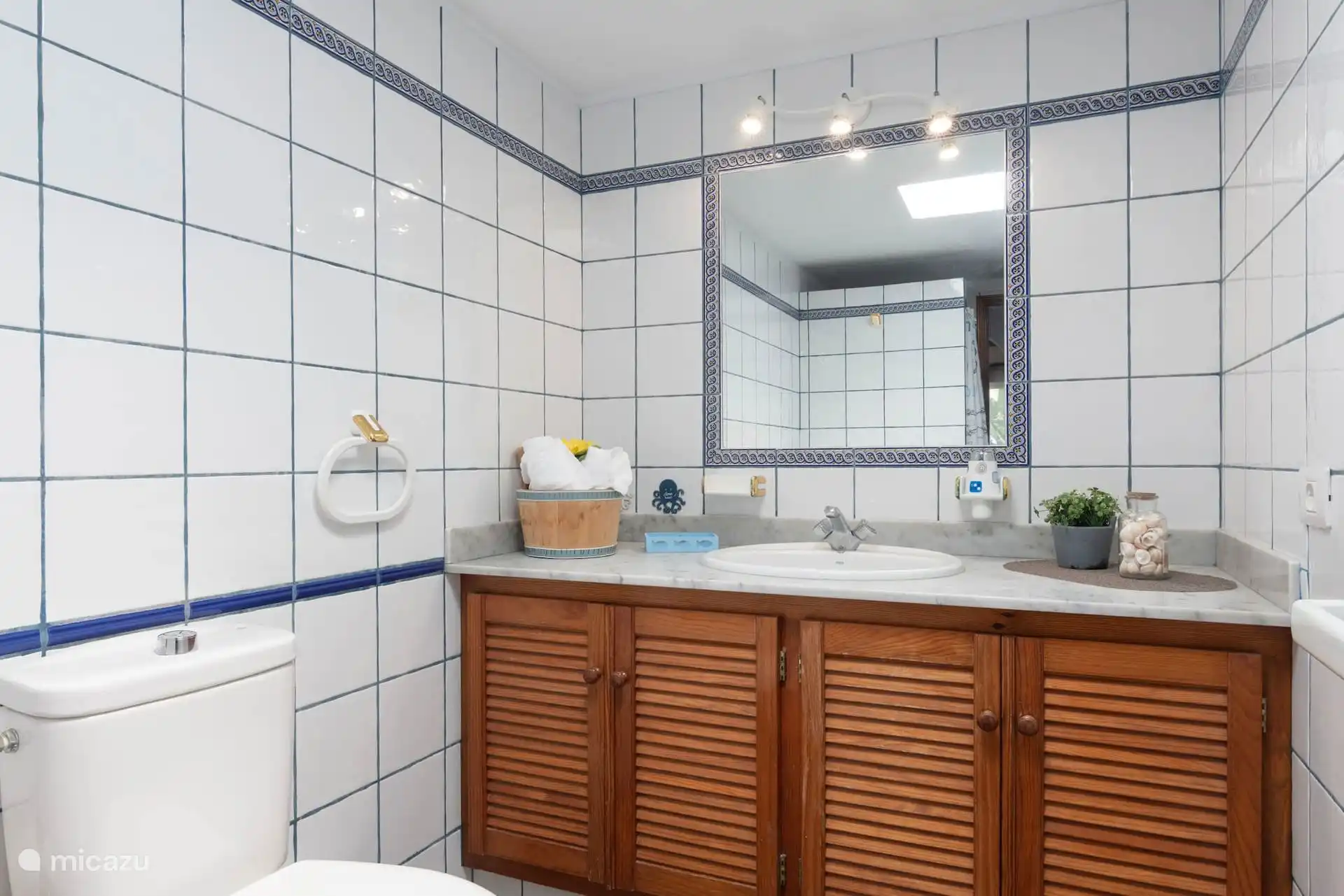 Salle de bain avec lavabo sur placard en bois, plan de travail en marbre et miroir encadré de carrelages.