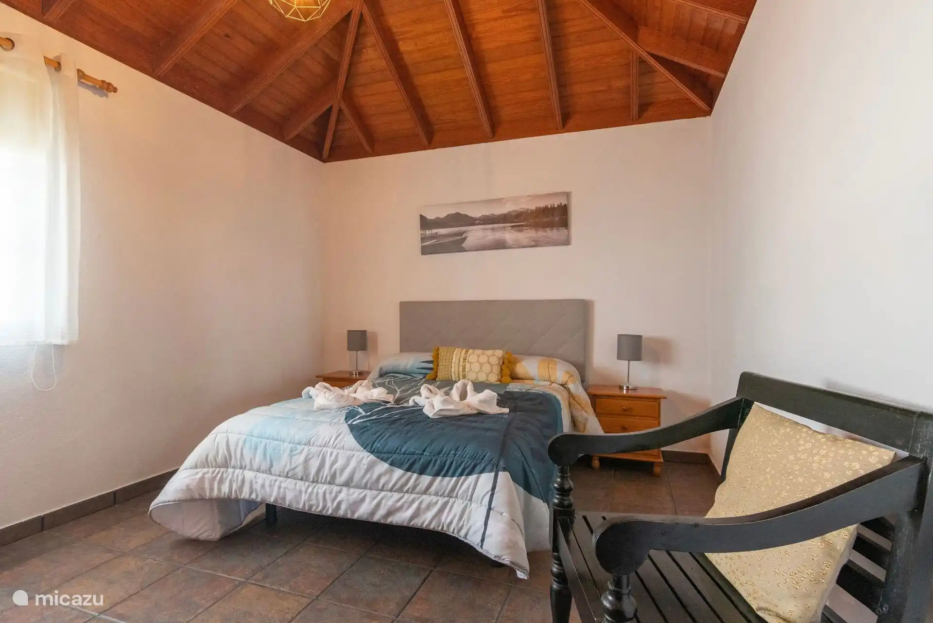 Chambre avec lit double, tables de chevet avec lampes de chaque côté et un banc en bois à côté du lit.