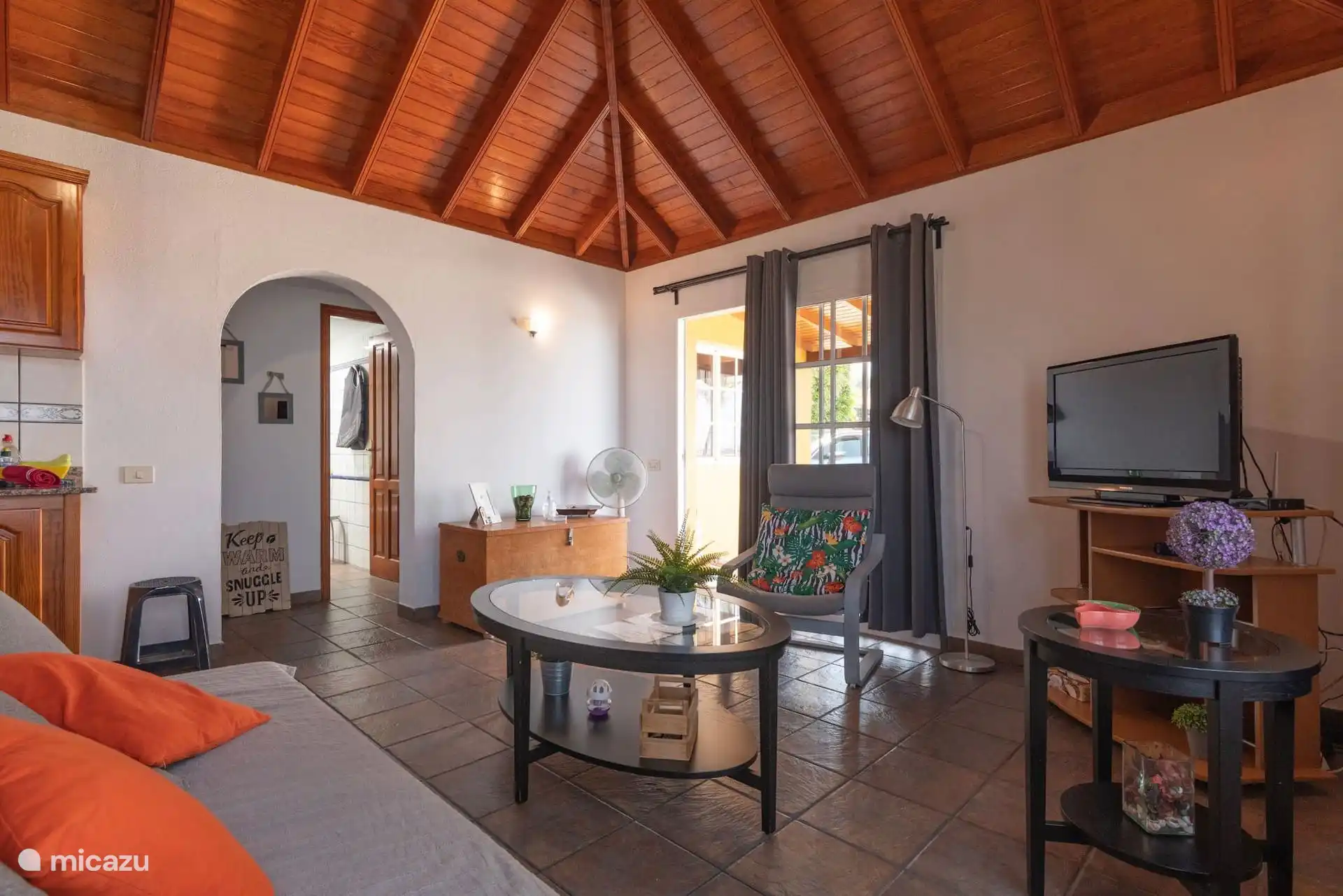 Une autre vue sur le salon, avec le fauteuil à côté de la porte du porche et, à gauche, l’arche qui surplombe le couloir des chambres.