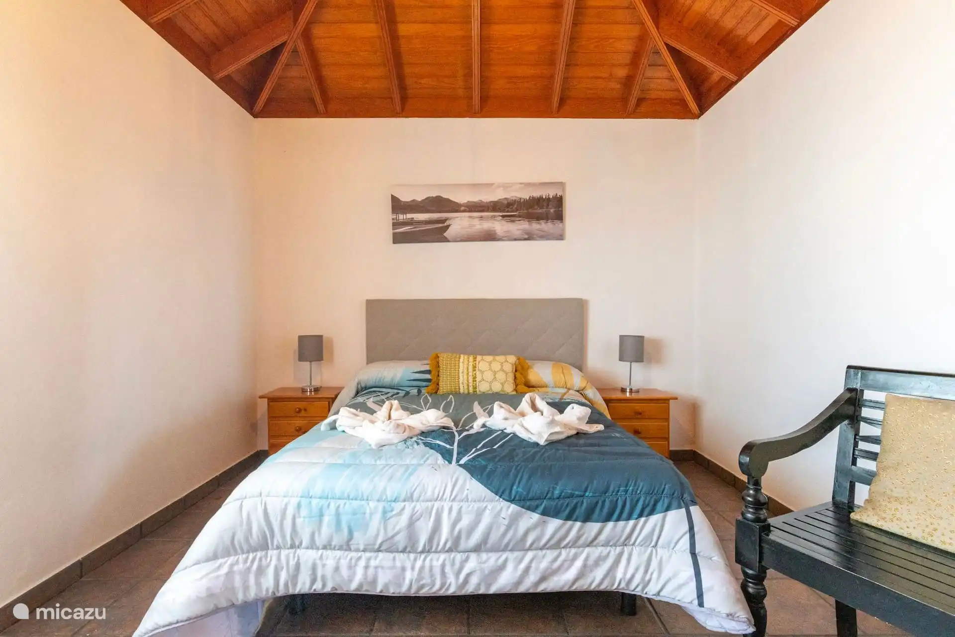 La même chambre devant, avec le lit centré sous le tableau et le plafond en bois à croupe.