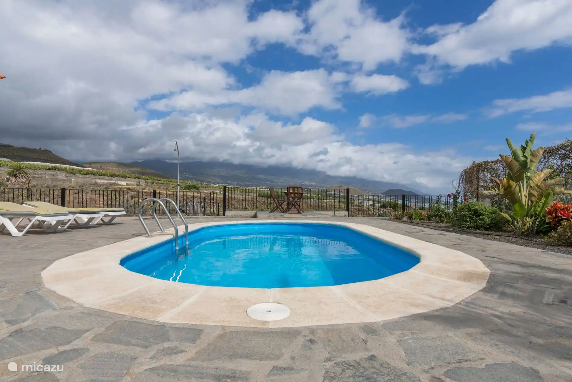 The swimming pool with the outdoor shower next to it and, behind the railing, the banana trees and the mountain between clouds.