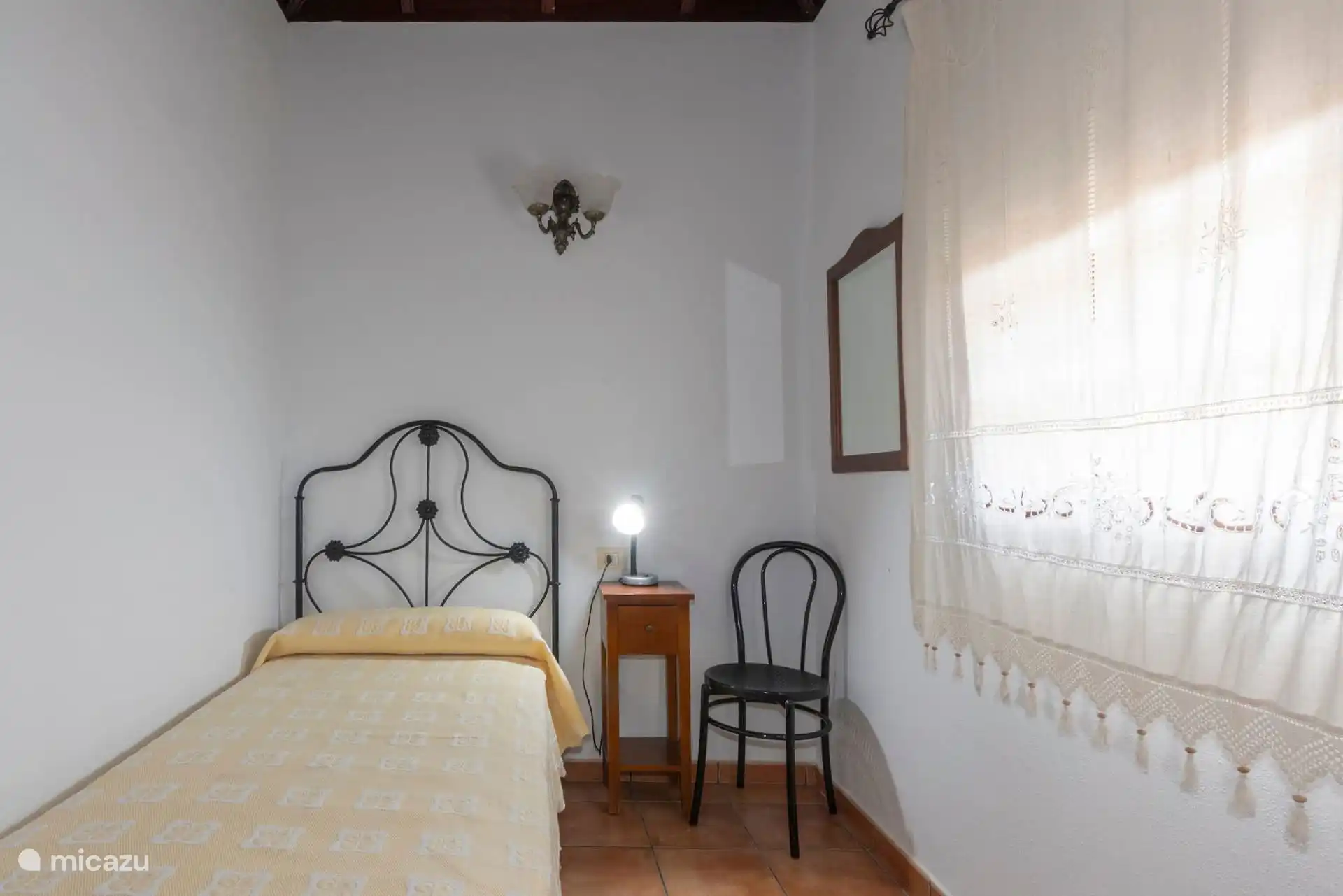 The single bedroom from the door, with the chair and mirror by the window.