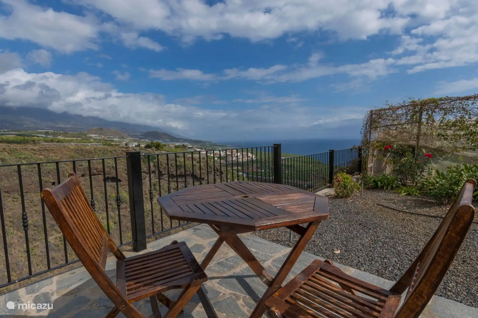 Folding wooden table with two chairs next to the railing, overlooking the ravine, the banana trees and the sea.