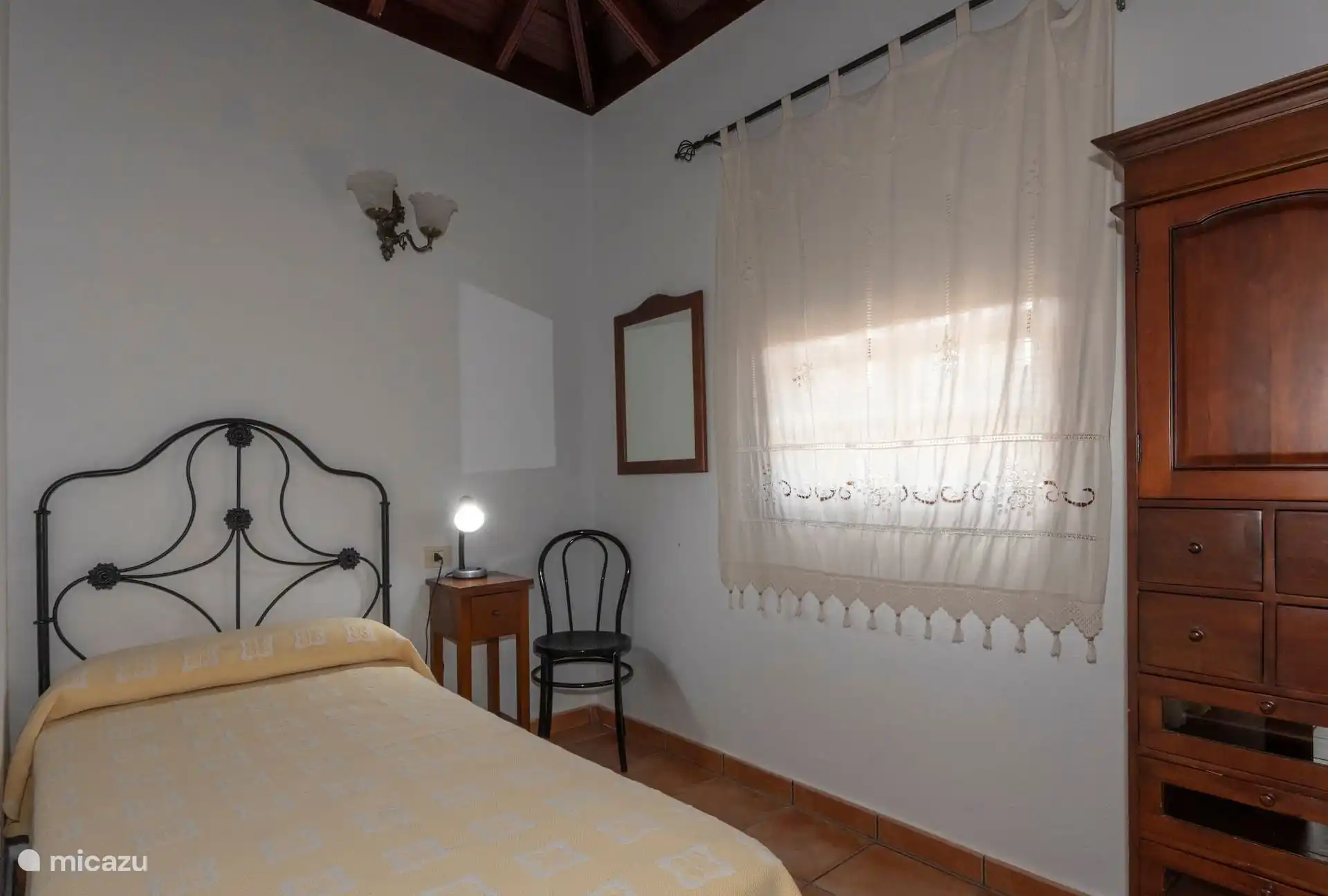 Bedroom with a single bed, bedside table and wooden wardrobe, also under tea beamed ceiling.