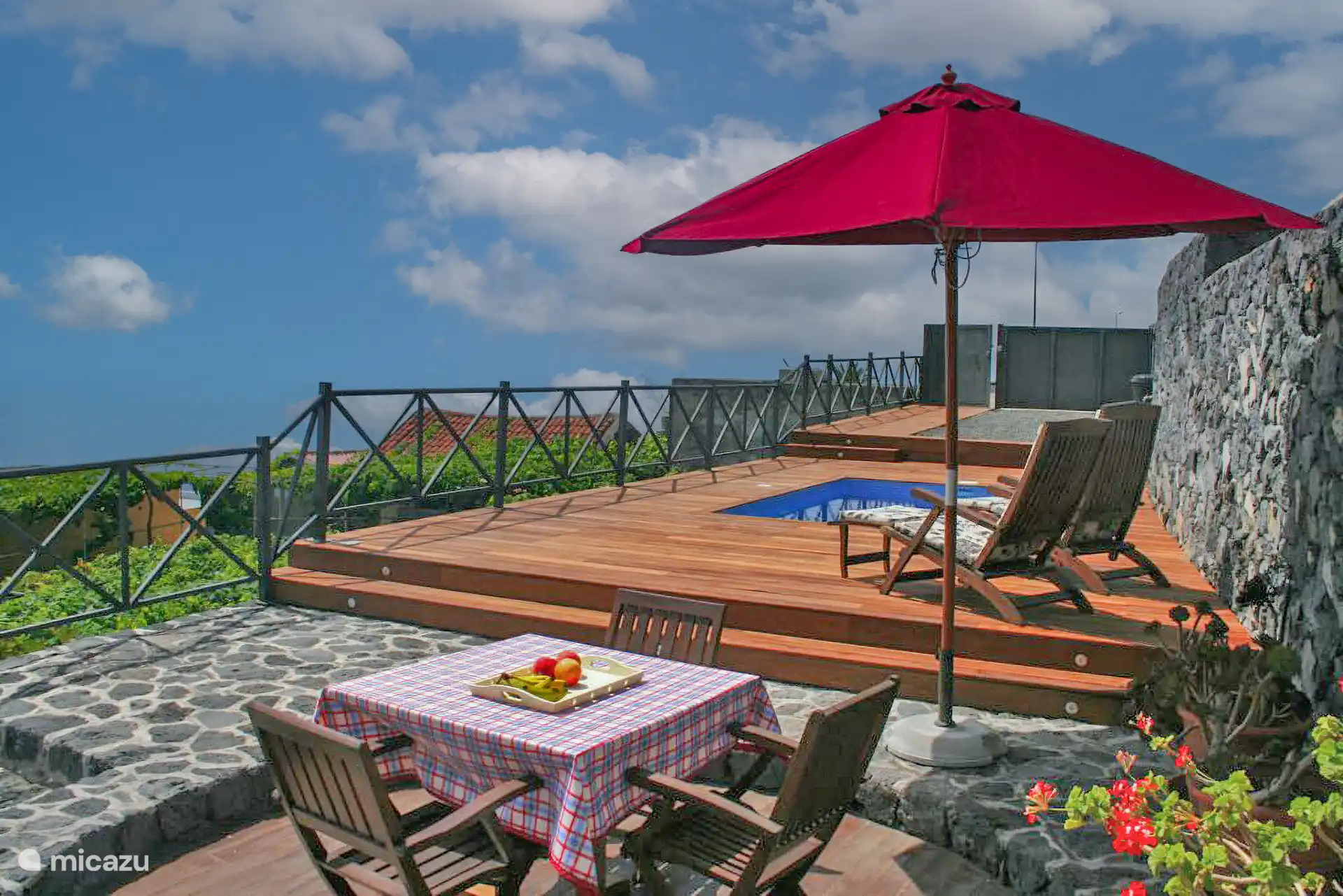 tafel met tafelkleed en parasol naast het zwembadterras; aan de andere kant van de reling de wijngaarden.