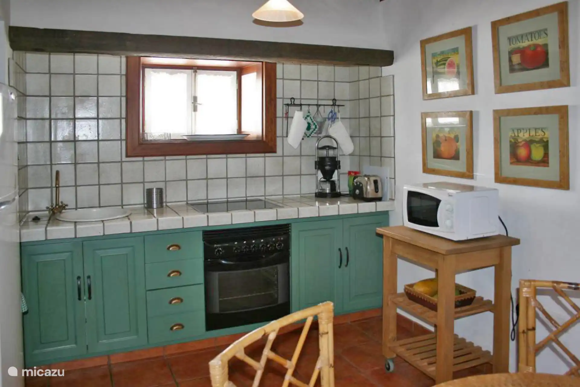 Keuken met keramische kookplaat, oven en gootsteen op betegeld aanrecht; De magnetron, op een houten bijzettafeltje.