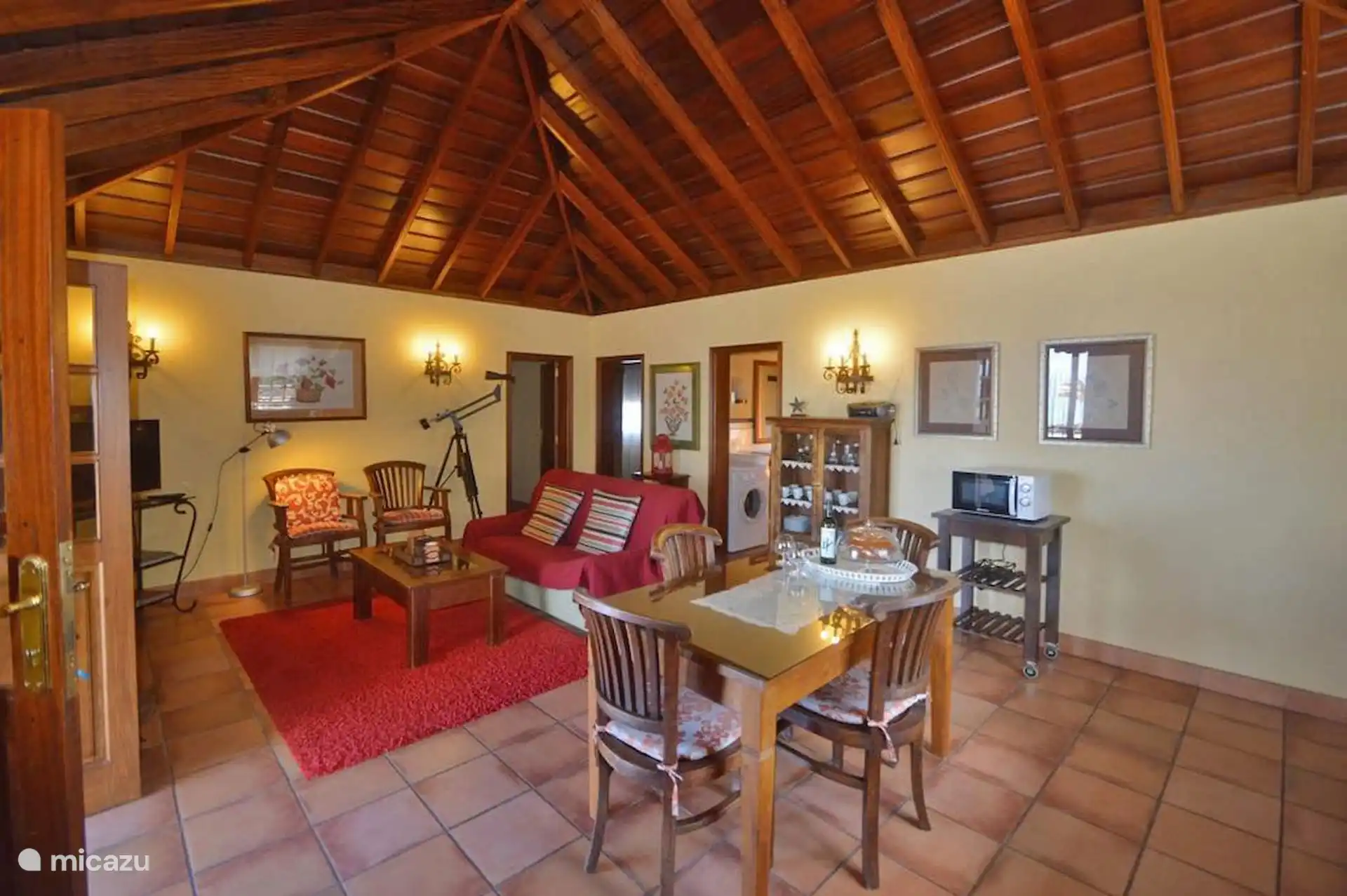 The living-dining room from the entrance: table for four, sofa, armchairs, display cabinet with crockery and microwave on a side table.