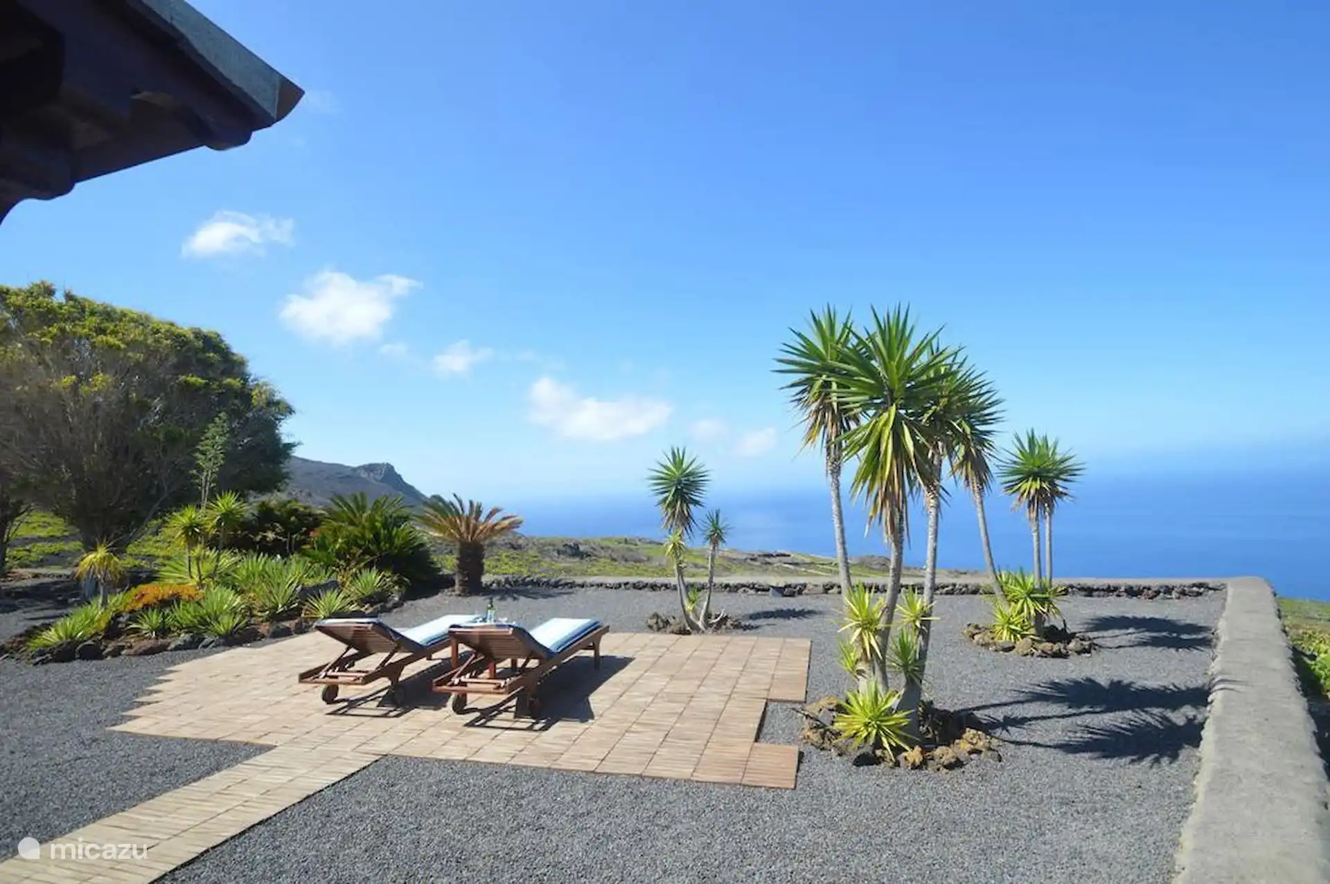 Sun lounger area on wooden decking, surrounded by picón and dracenas, with the sea in the background.