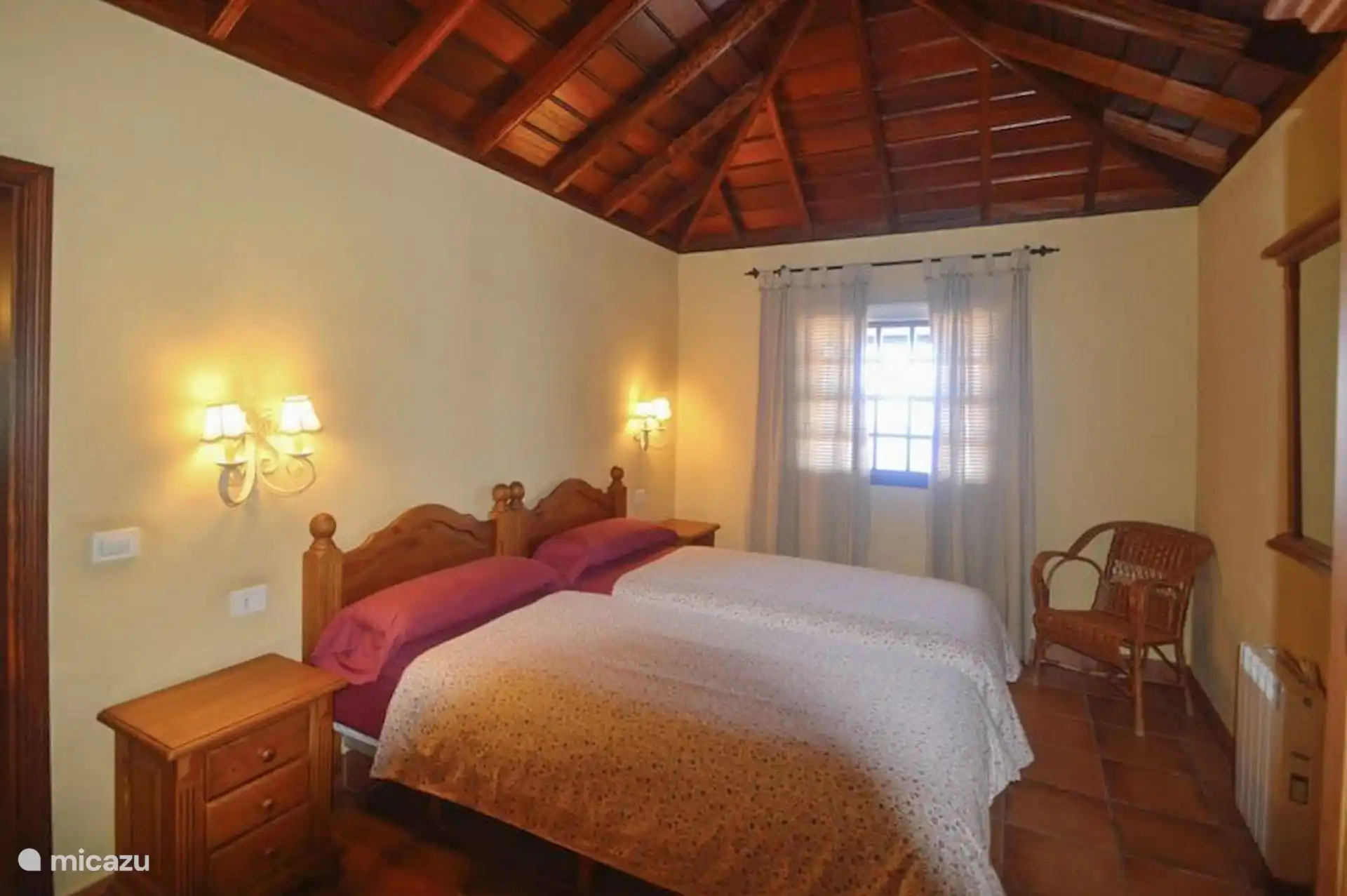 The other bedroom, with two single beds joined together, wooden bedside tables and a wicker armchair next to the window.