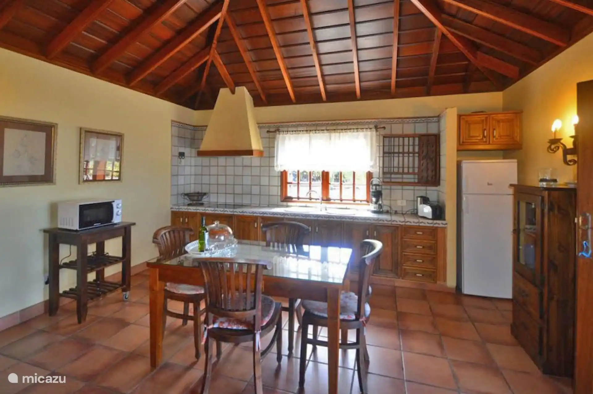 The kitchen, with ceramic hob, sink under the window, fridge, toaster, coffee maker and microwave; in front, the table with four chairs.