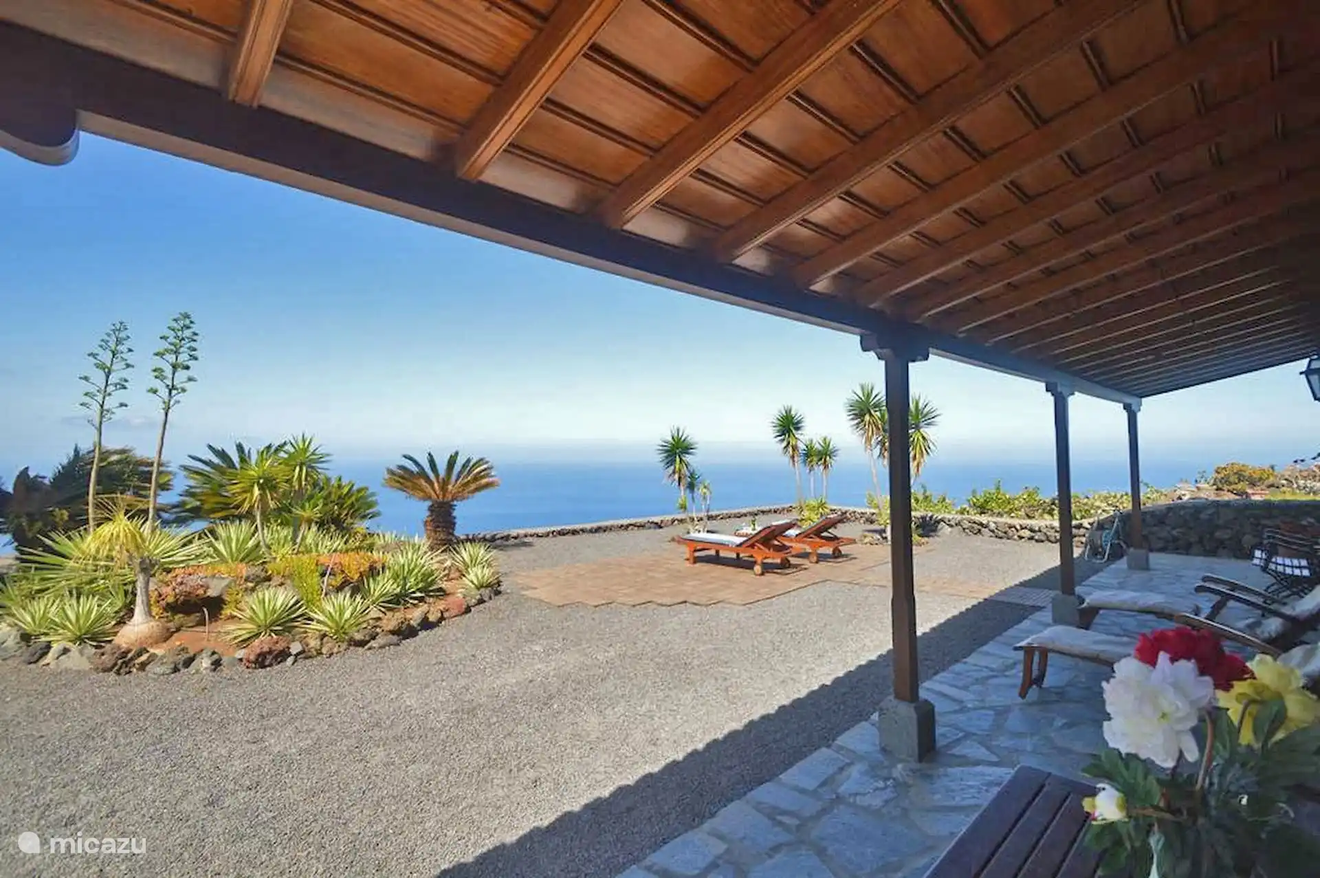 The porch, with its wooden roof, opens to the garden of succulents and palm trees and the sea line.