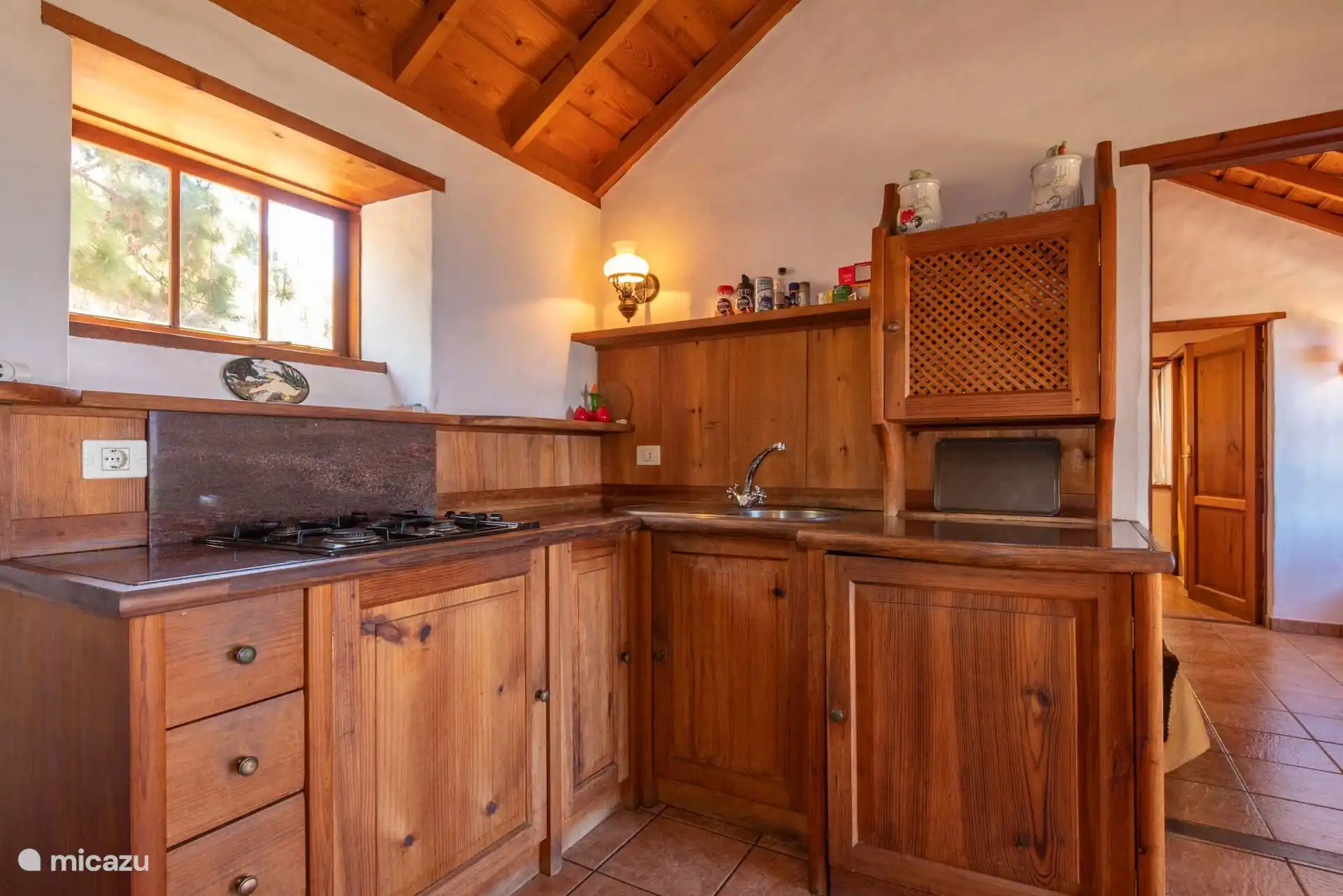 Houten L-vormige keuken met gasfornuis, gootsteen en magnetron; op de achtergrond, de doorgang naar de slaapkamer.