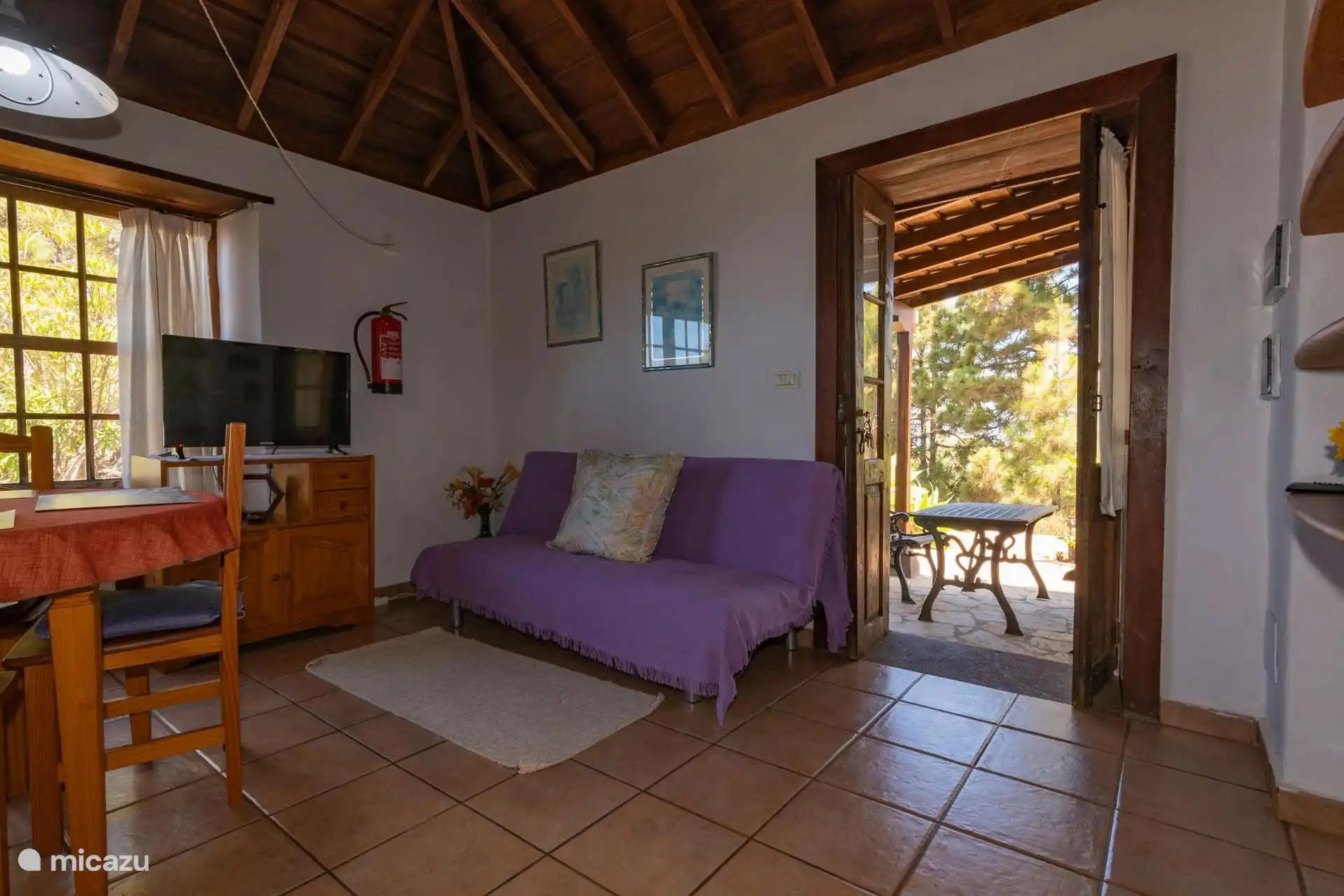 The living room from the other end: sofa, television and the door open to the covered terrace at the entrance.
