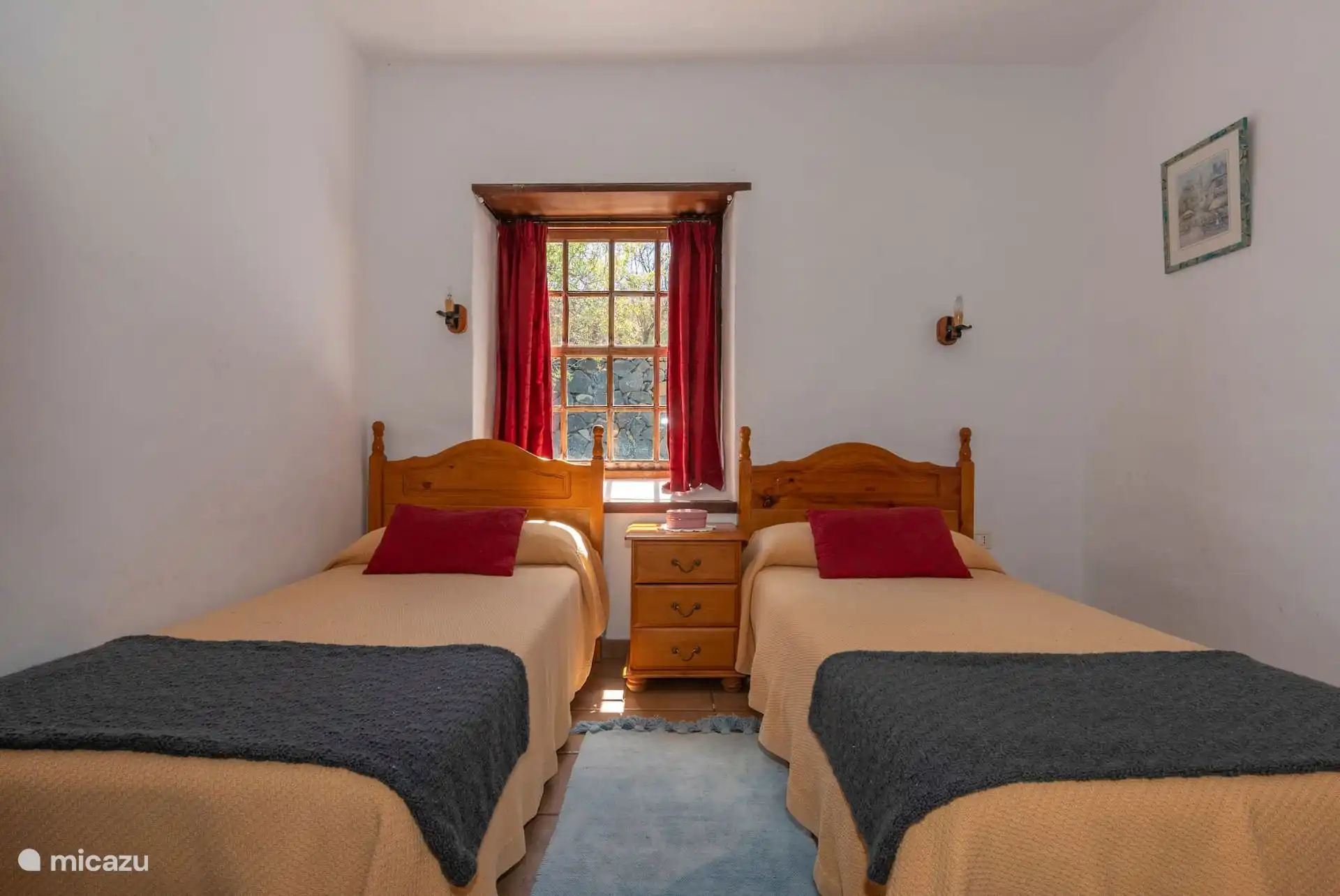The same bedroom in front: the two beds separated by the bedside table, under the red-curtained window.