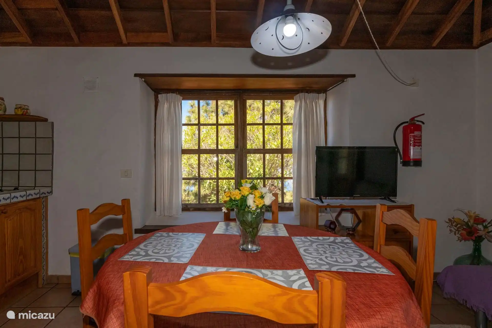 The dining room in front: table set for four, television and the wooden window that overlooks the vegetation.
