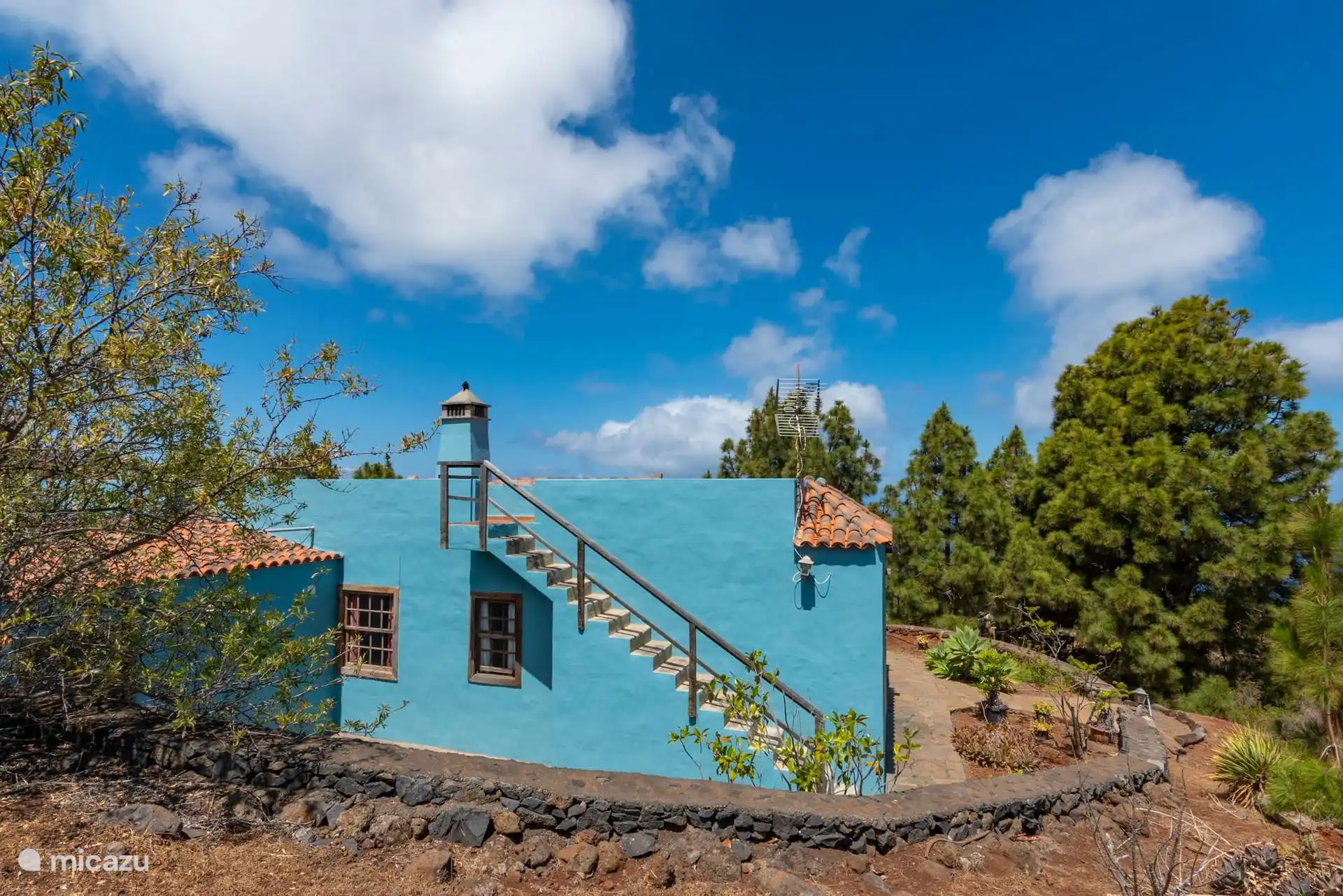 Side of the house with the staircase that goes up to the roof, next to the volcanic stone wall.