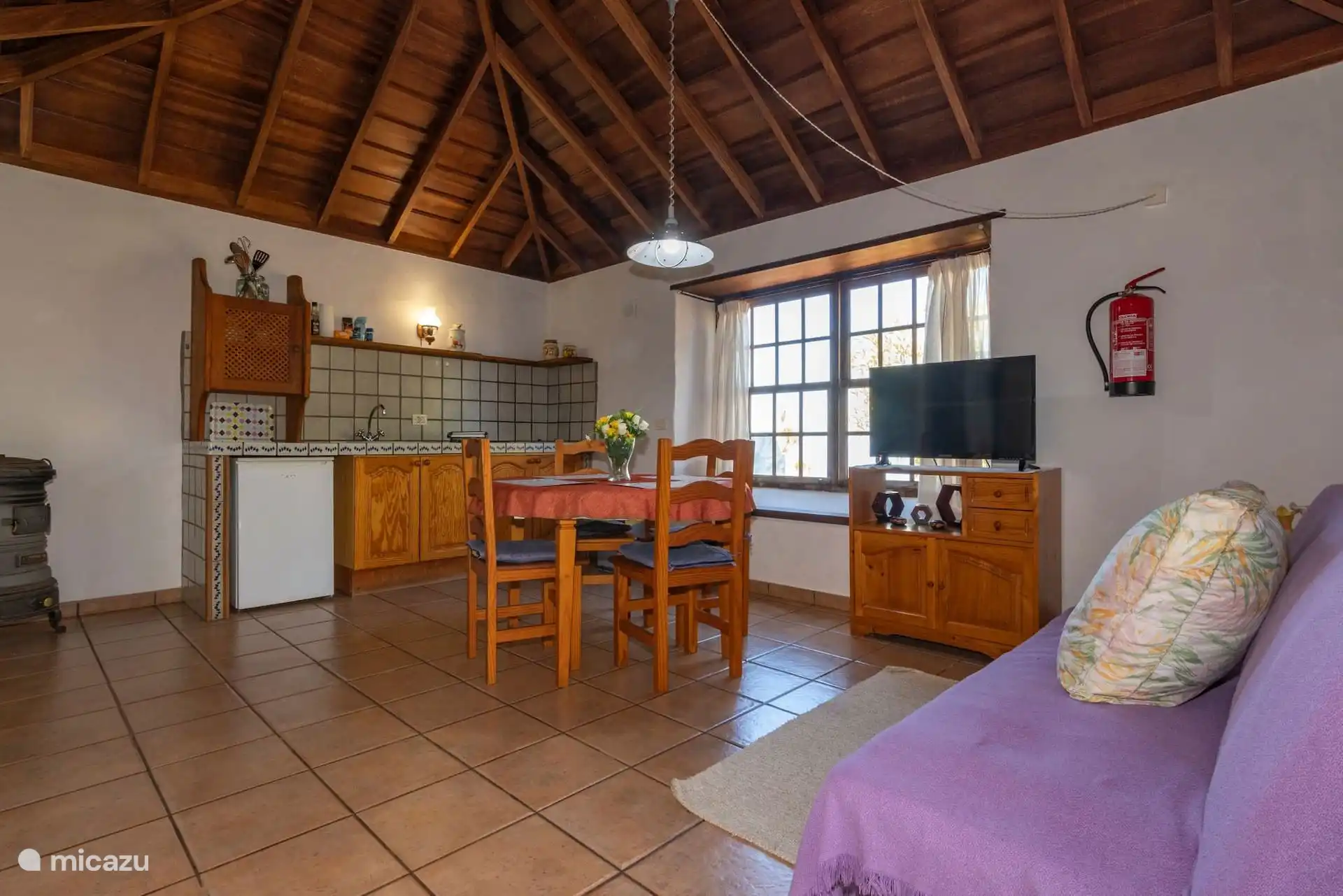 Living room, dining room and kitchen in the same space, under the gabled wooden roof; on the left, the wood stove.