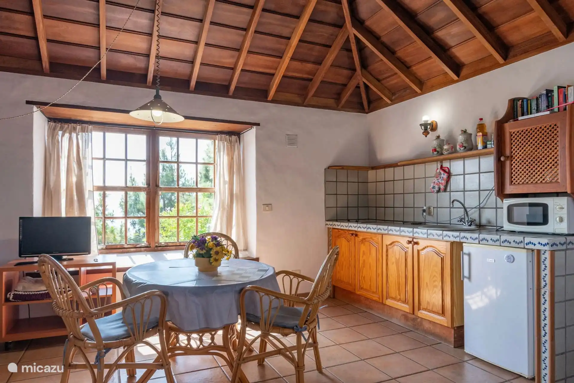 Der gleiche Bereich zur Küche: geflieste Arbeitsplatte mit Spüle, Mikrowelle und Kühlschrank sowie der runde Tisch am Fenster.