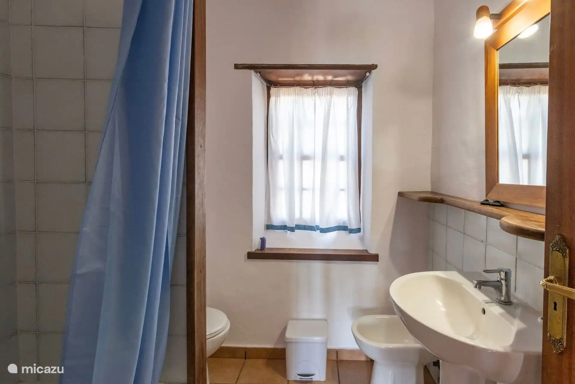 Badezimmer mit Waschbecken, Spiegel, Toilette, Bidet und Badewanne hinter dem Vorhang; Fenster mit Vorhängen.