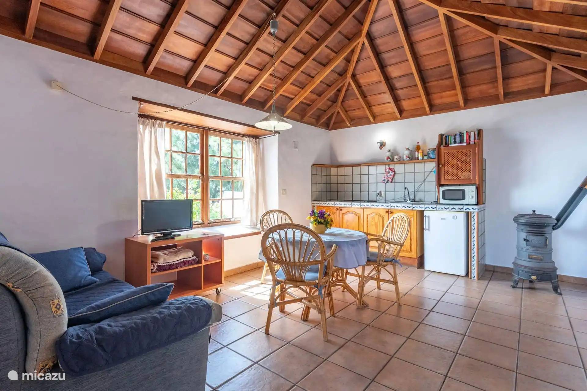 Volle Sicht auf das Wohnzimmer mit integrierter Küche, dem Holzofen rechts und dem Walmteedach.