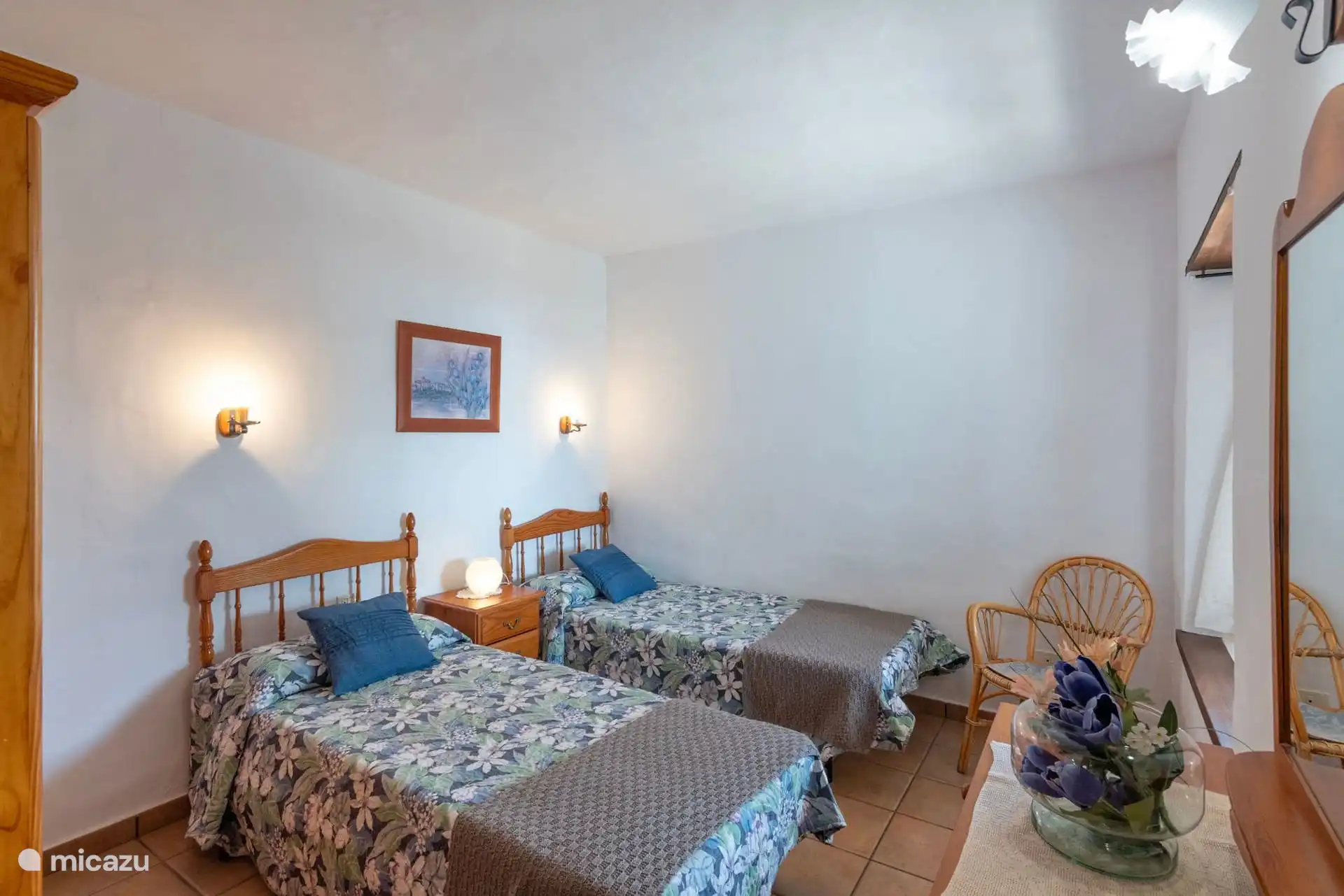 Dasselbe Schlafzimmer von der Tür aus, mit Korbstuhl und Spiegel am Fenster.