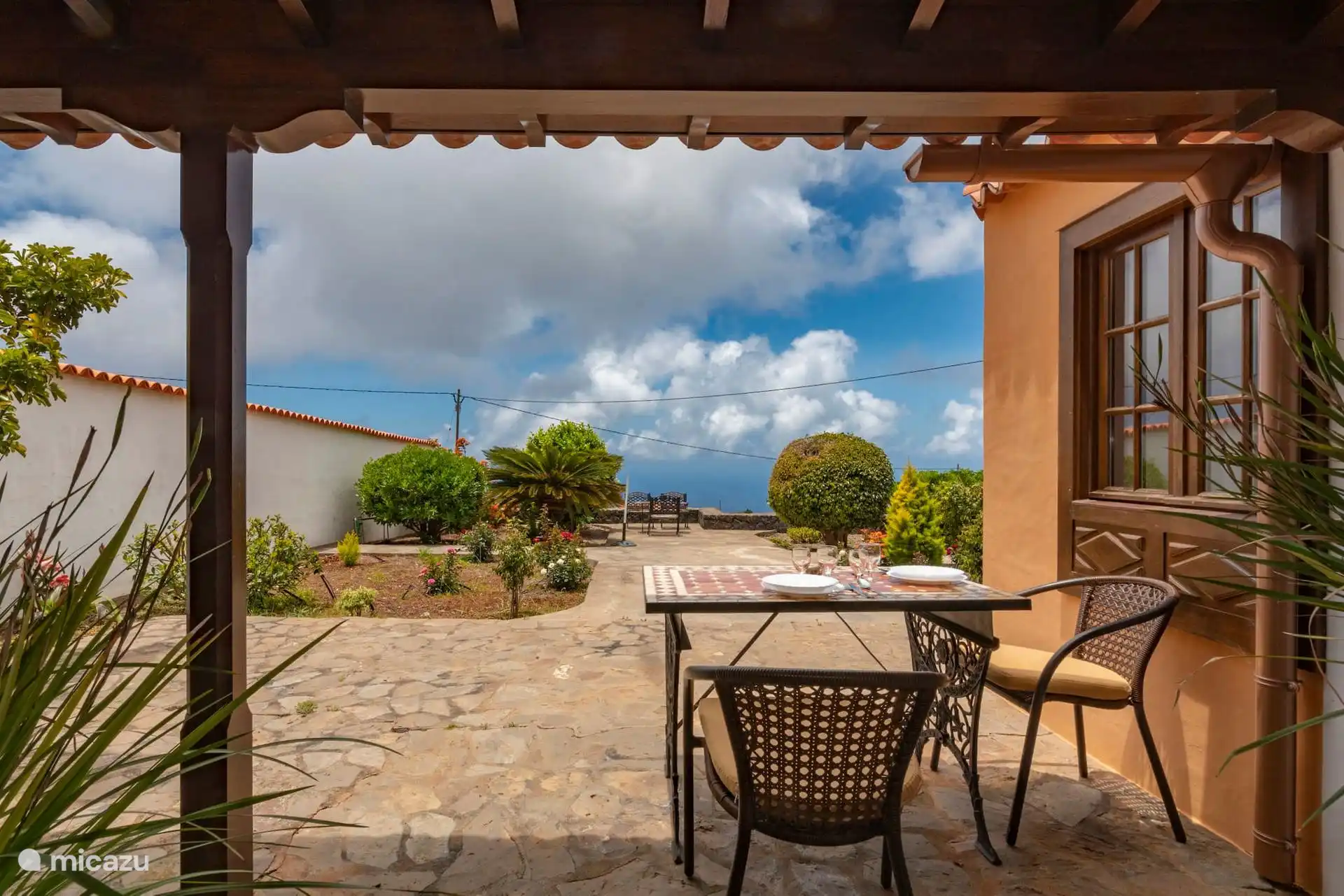 Wrought iron table under the porch, with the garden in front and the sea on the horizon.