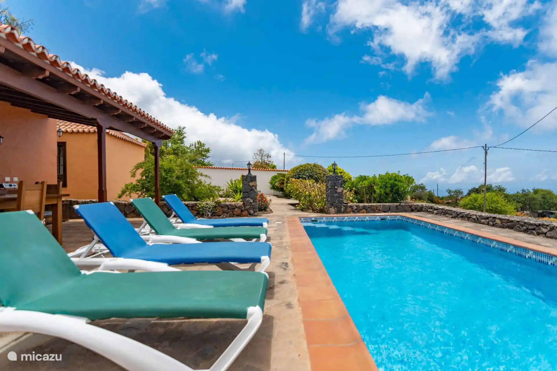 Loungers by the pool; on the left, the barbecue porch, and around it, the volcanic stone wall.