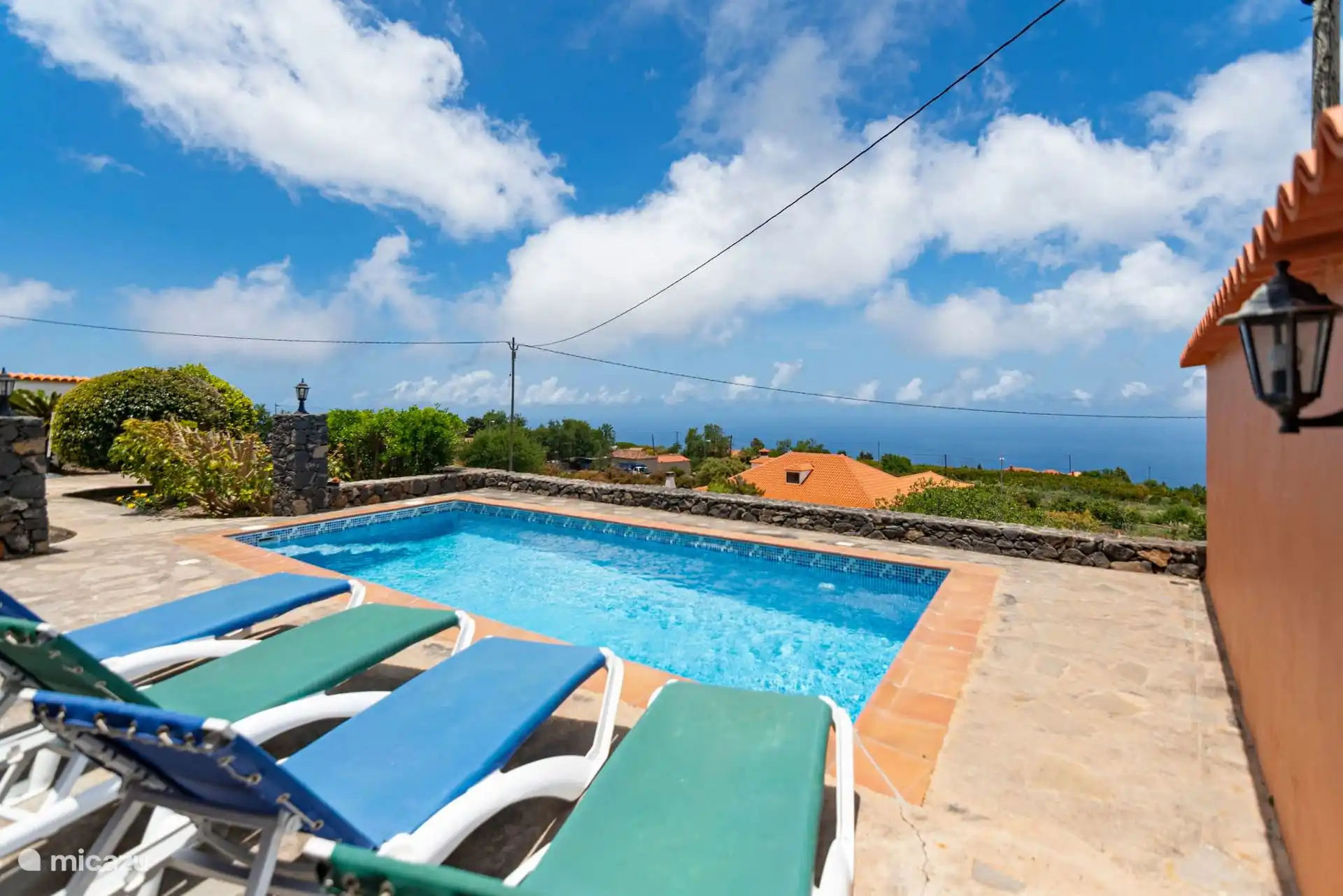 The swimming pool looking out to sea over the volcanic stone wall; below, the roofs of the neighboring houses.