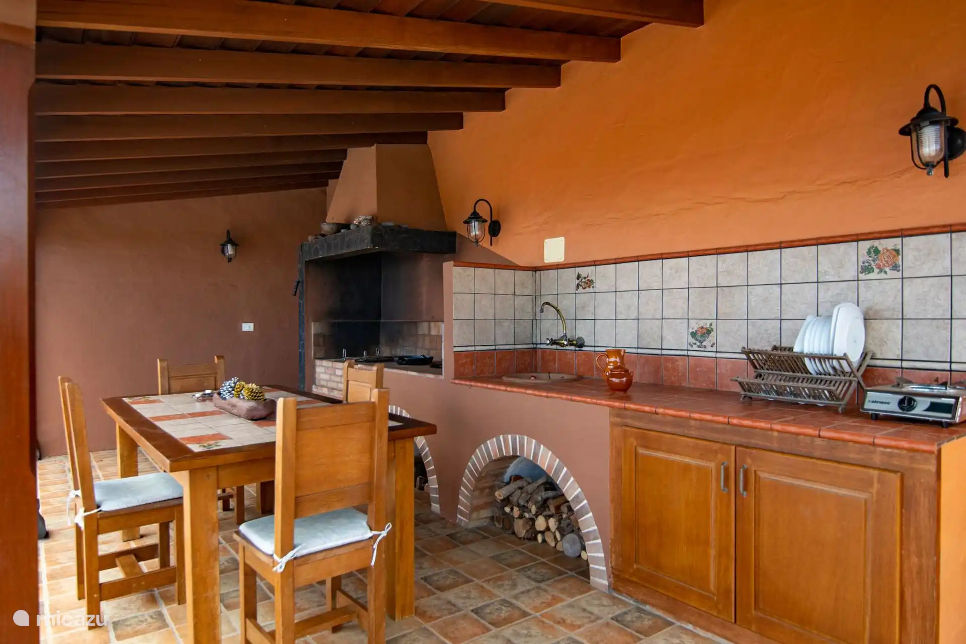 Covered outdoor kitchen: built-in barbecue with hood, woodshed under the brick arch, built-in sink and wooden table.