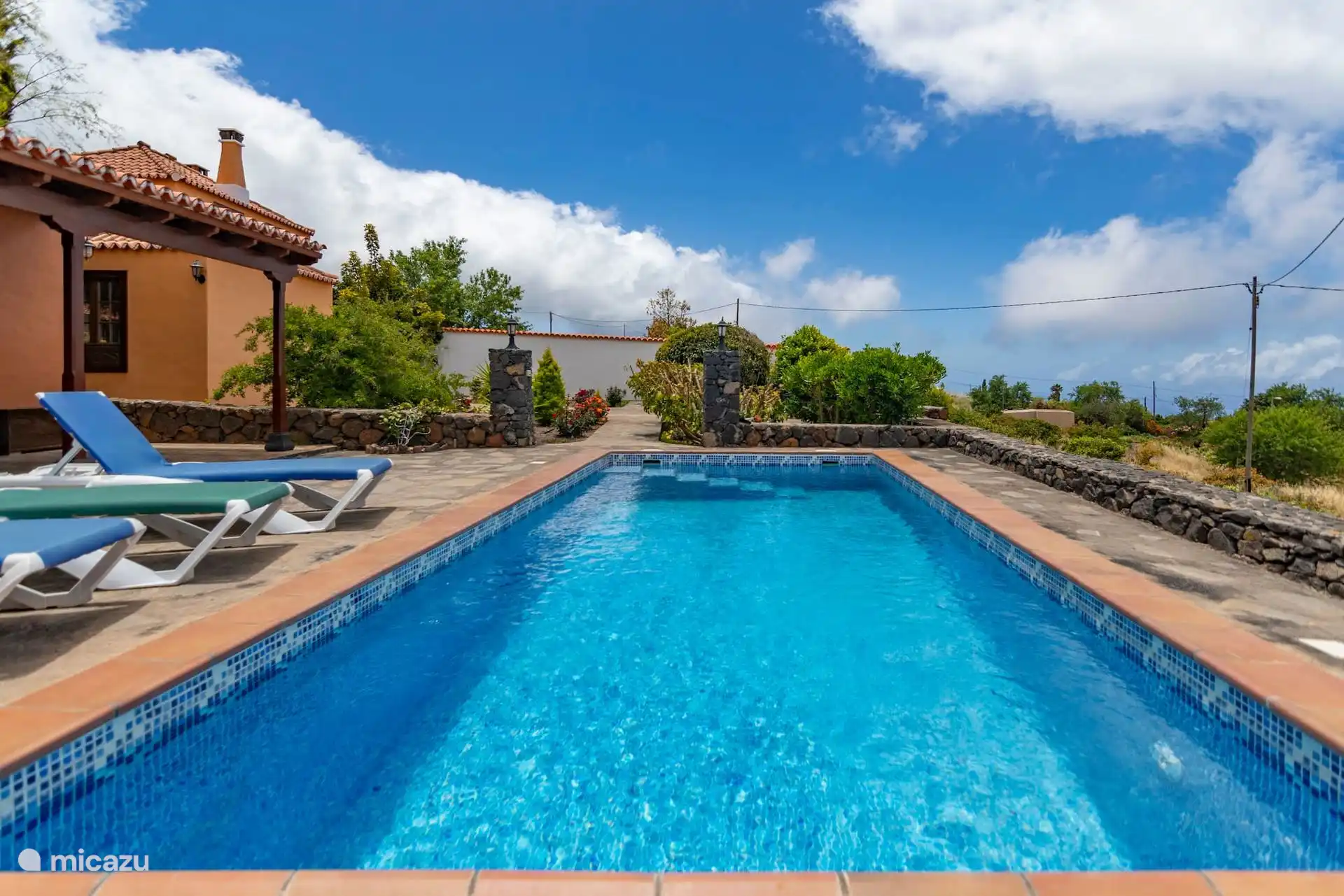 The swimming pool lengthwise, with the house on one side and the volcanic stone wall that encloses the plot.