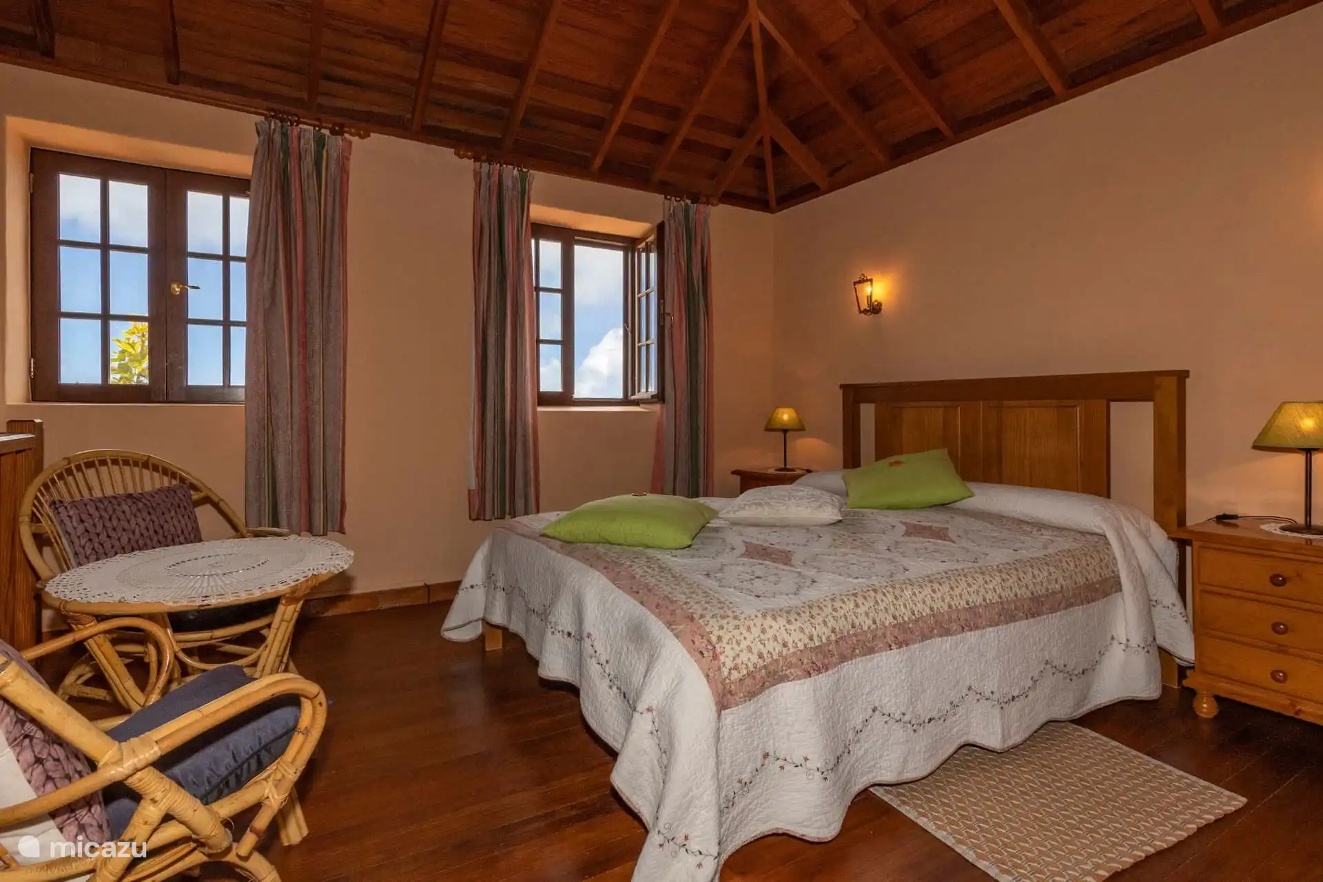 Another view of the master bedroom, with its two windows and wicker armchairs in the foreground.