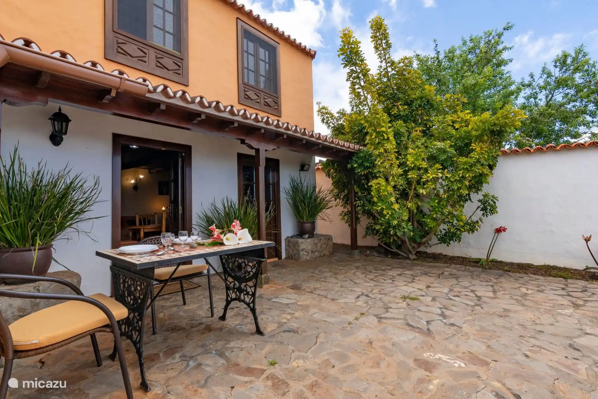 Cobbled patio with wrought iron table by the living room door; Upstairs, the upper floor with wooden windows.