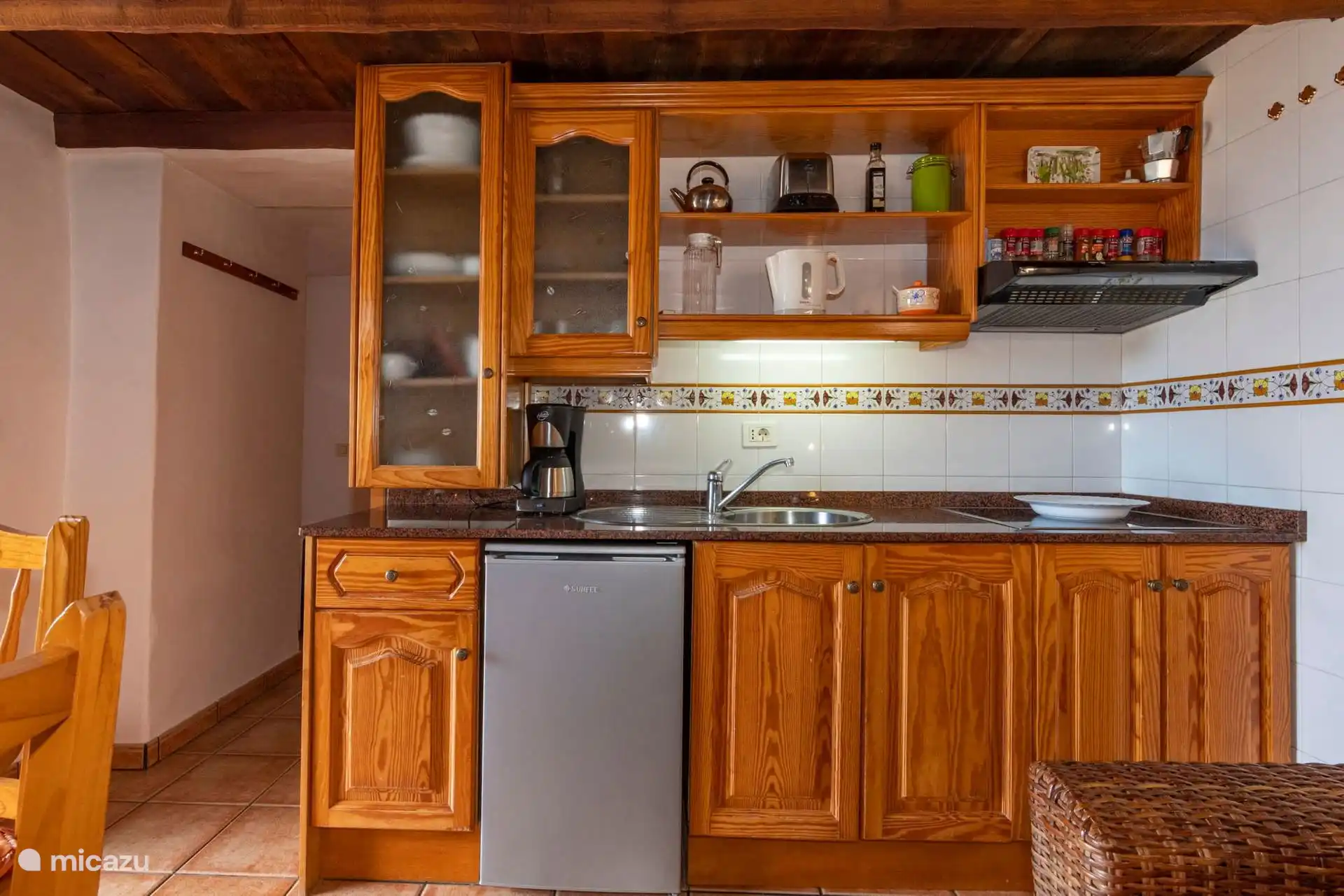 Kitchen detail: ceramic hob, sink, undercounter fridge and coffee maker; on the shelves, kettle, toaster and pots.