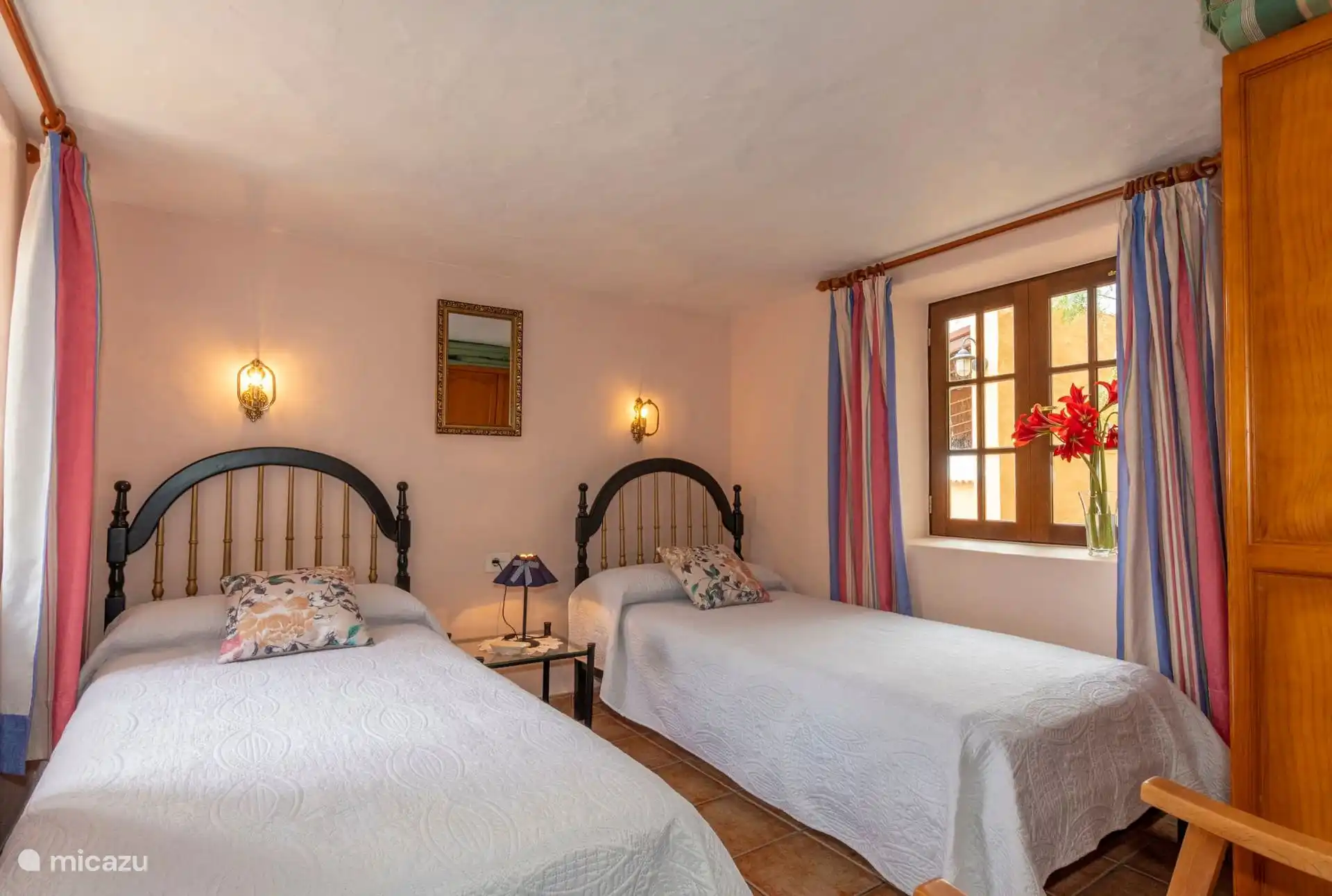 Bedroom with two single beds, black headboards with gold bars and mirror between the wall lights; Mud floor.