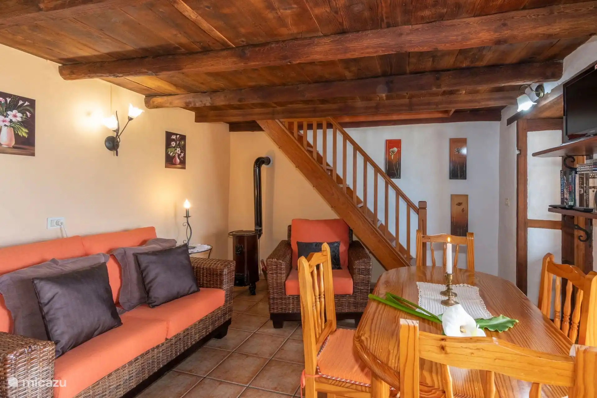 The living room from the other side: sofa and wicker armchair, wood stove and the wooden staircase that goes up to the upper floor.