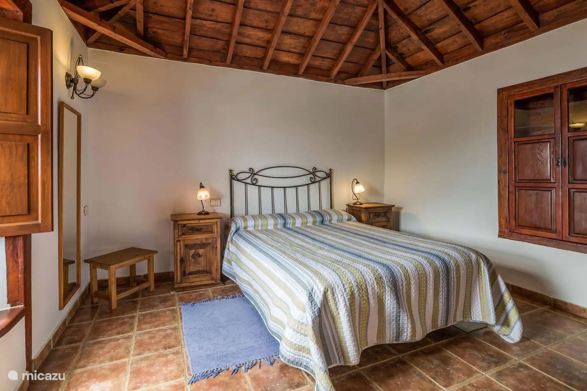 Slaapkamer met tweepersoonsbed, smeedijzeren hoofdeinde en twee nachtkastjes, onder het houten schilddak.