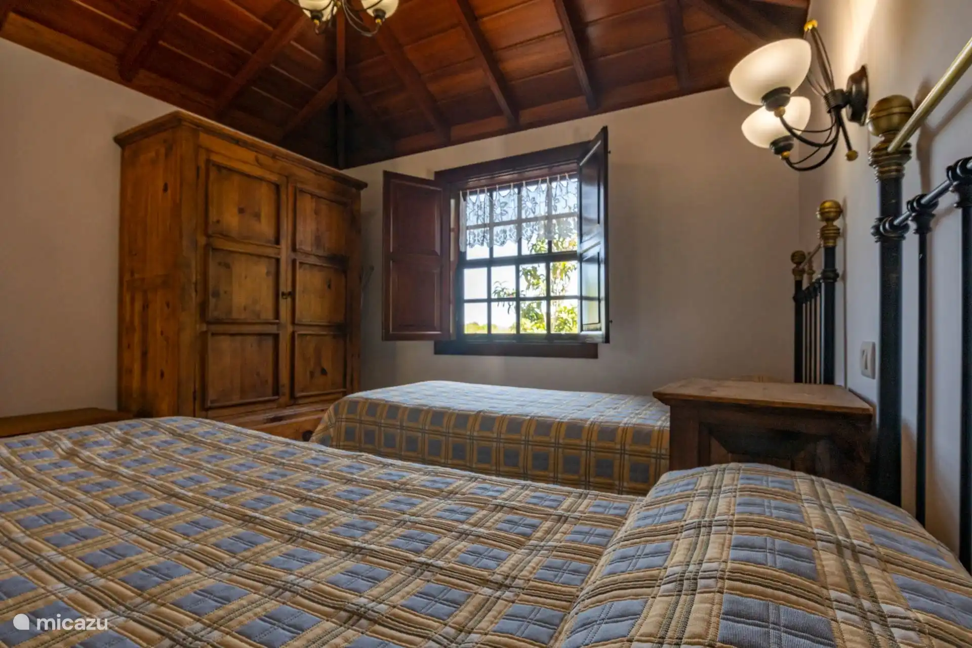 De slaapkamer heeft eenpersoonsbedden in de hoek, met de houten kast en het raam open boven het bed aan de achterkant.