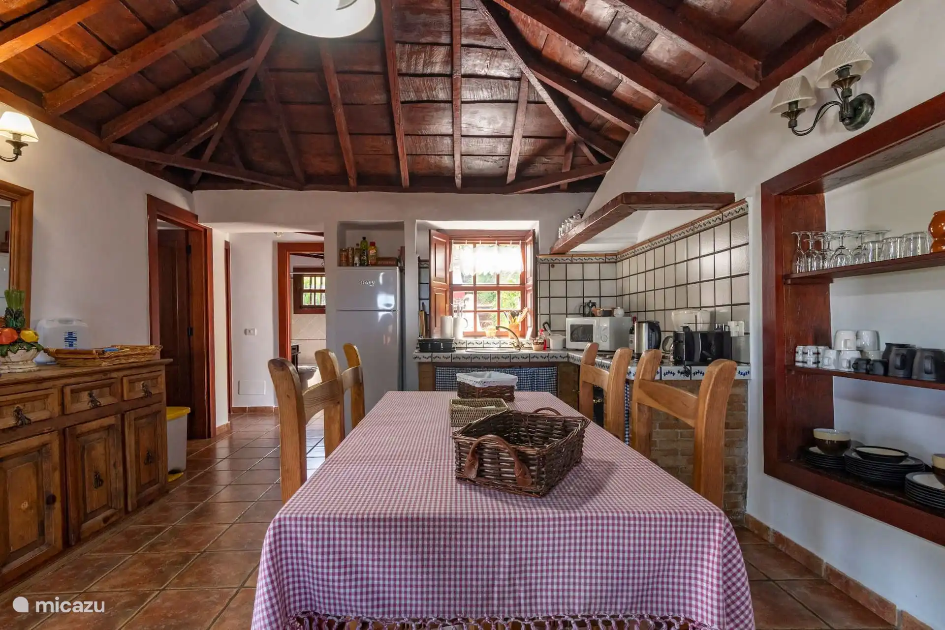 Dezelfde keuken als de eetkamer, met het dressoir, de kast met het servies en glazen, en de lange tafel in het midden.