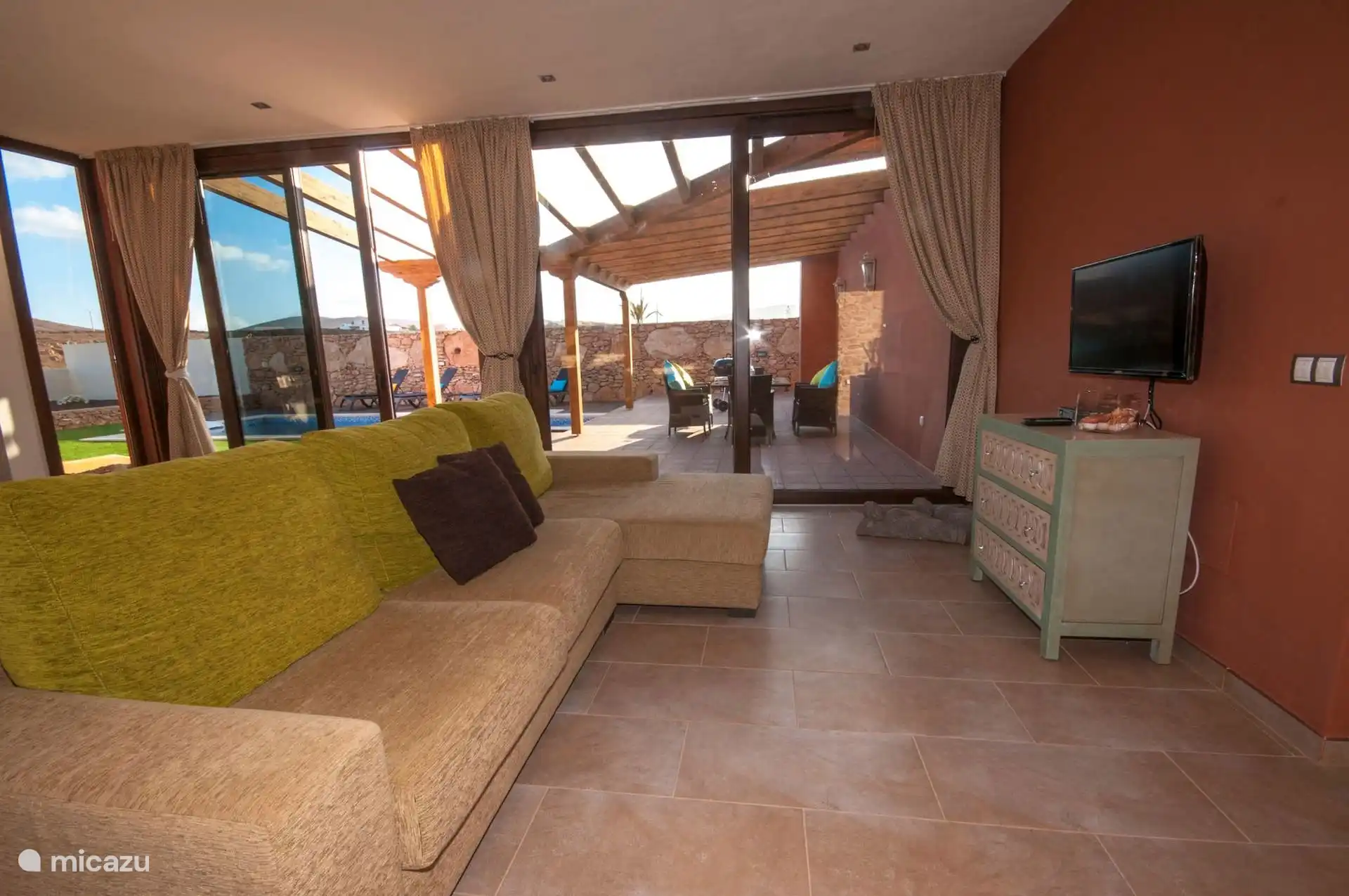 The living room from the other end, with the TV on the terracotta wall and the sliding doors open to the terrace.