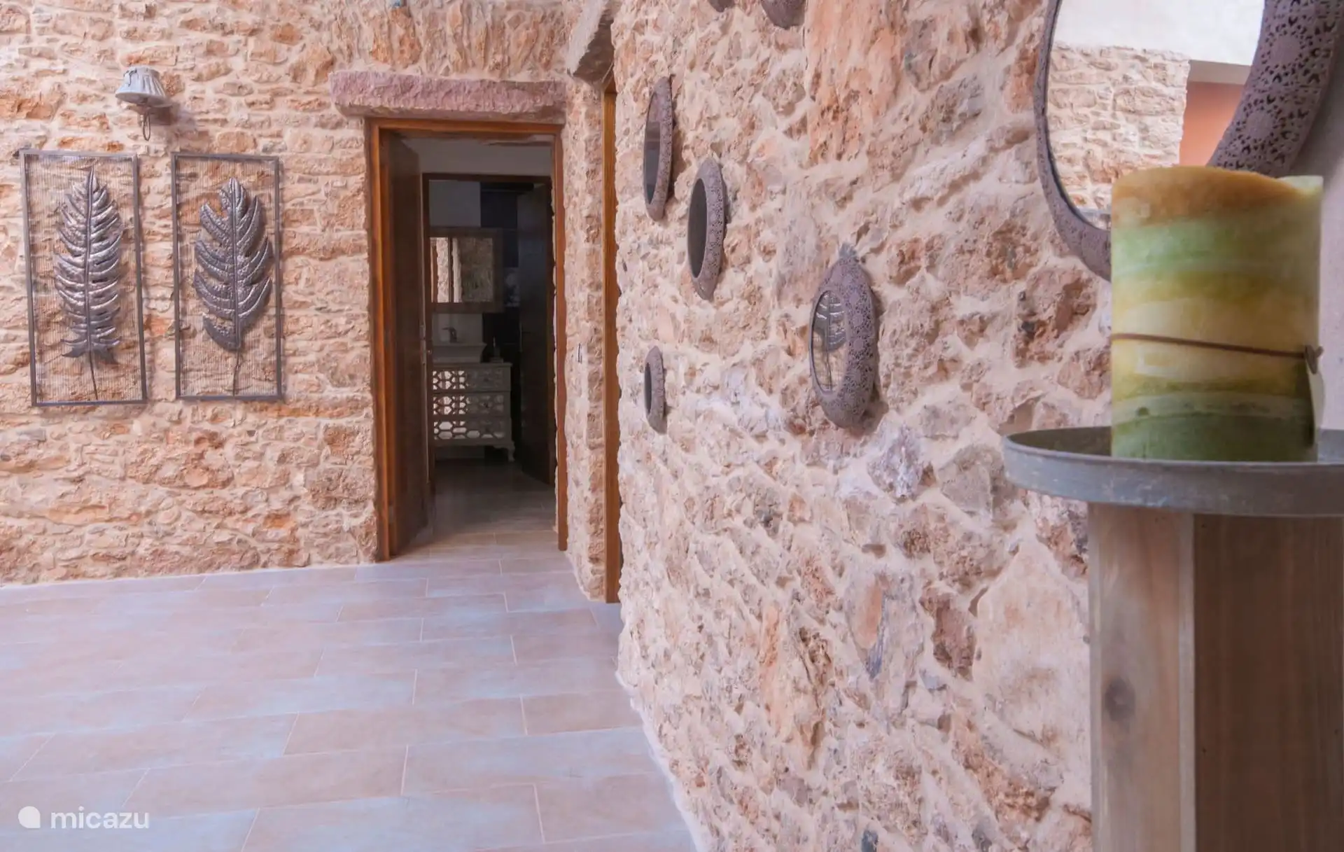 Exposed stone corridor with appliqués and decorative pieces; at the back, the door of one of the bathrooms.