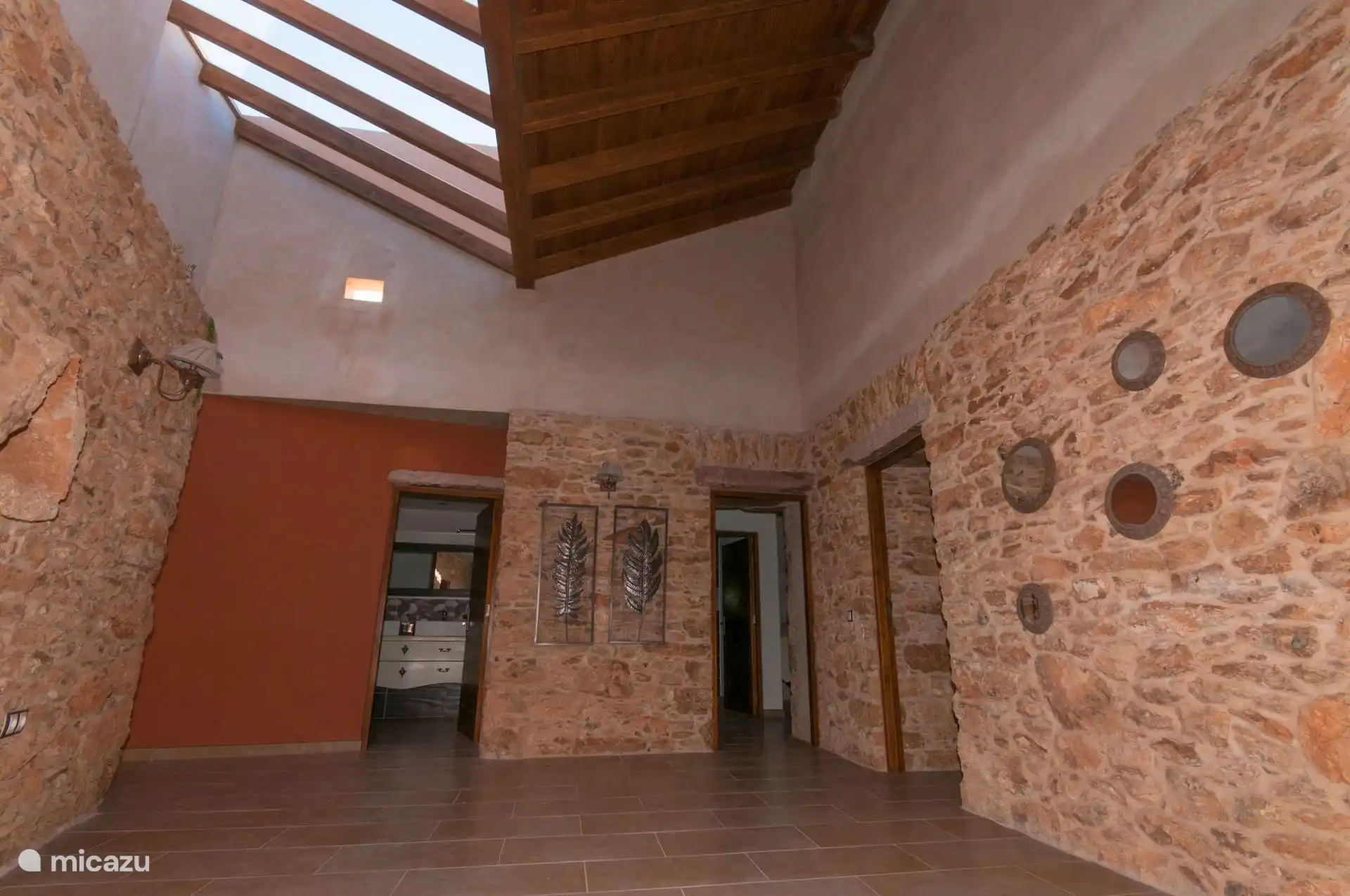 The entrance hallway, double height, with a skylight between beams and stone walls; on the sides, the bathroom and bedroom doors.