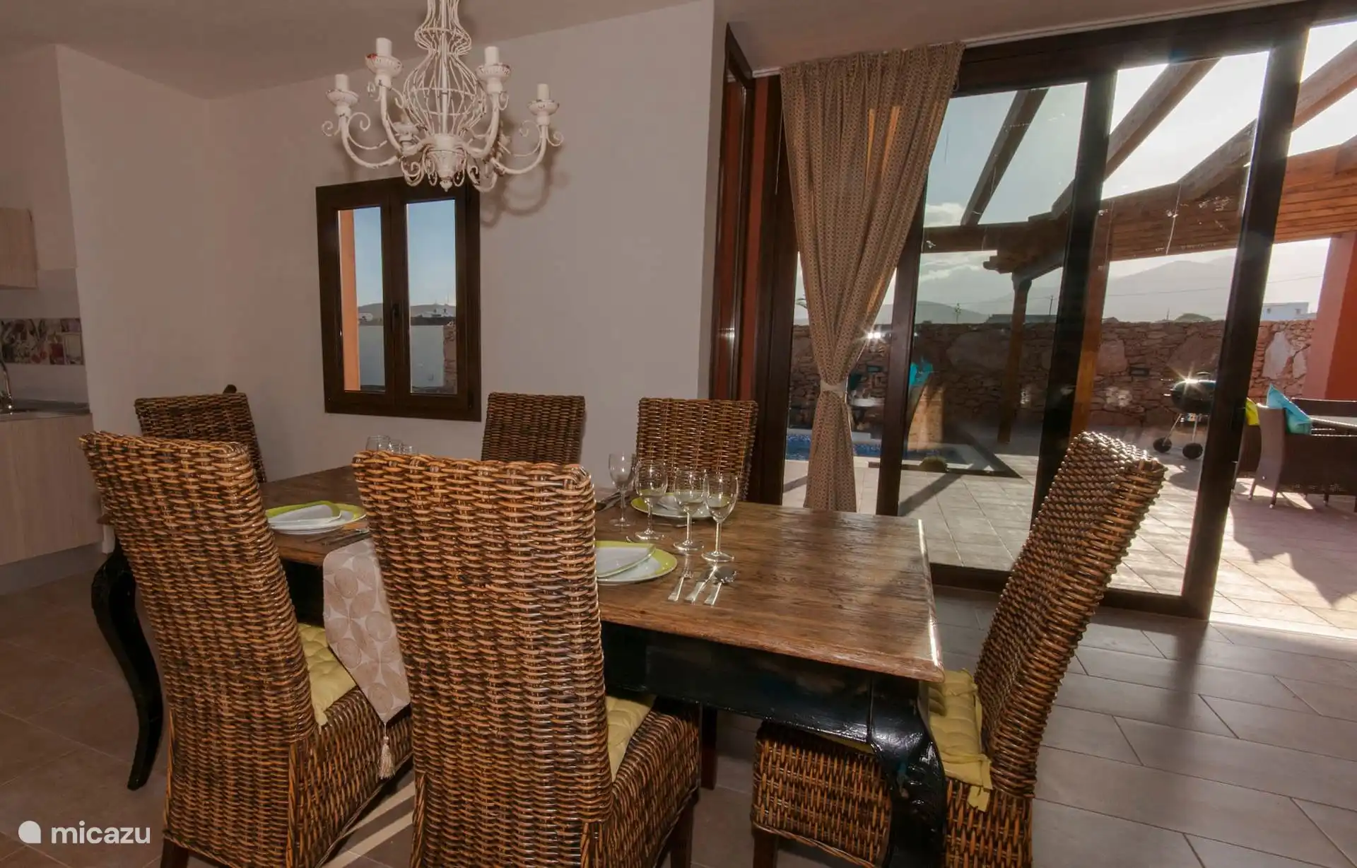 The dining table set for six, under the wrought iron lamp; The sliding door overlooks the terrace and the pool.