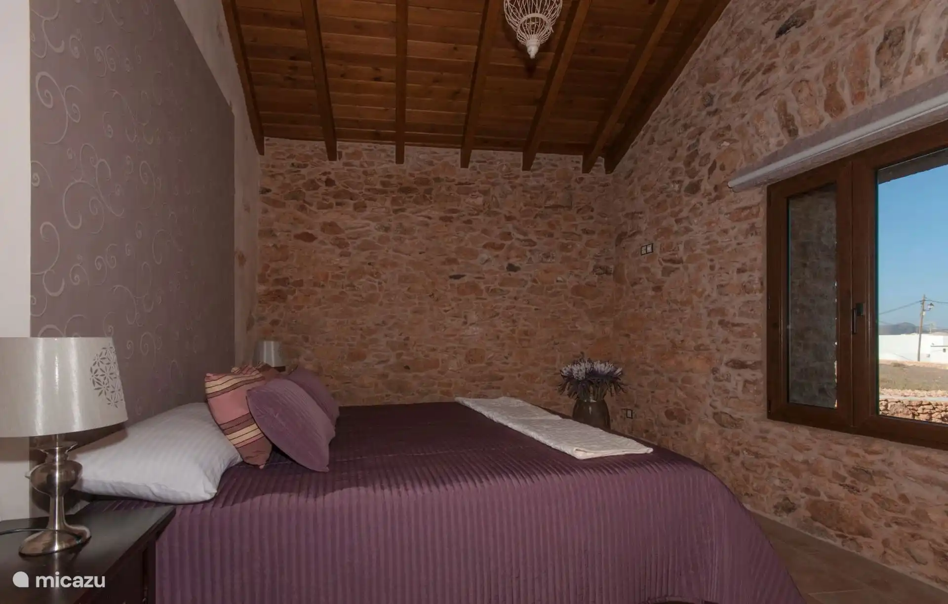 Another bedroom, with a double bed, wooden beamed ceiling and exposed stone wall.