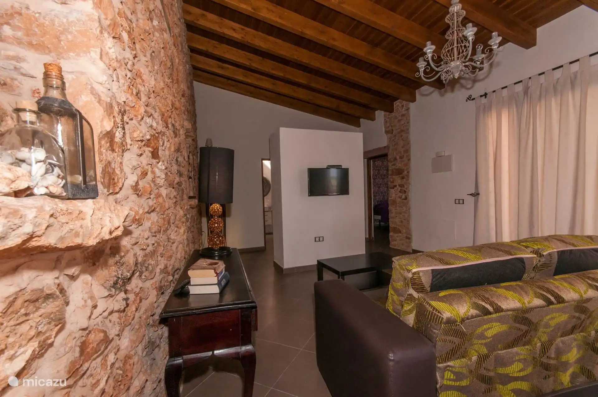 De woonkamer aan de andere kant, met de stenen muur op de voorgrond en het raam met gordijnen.