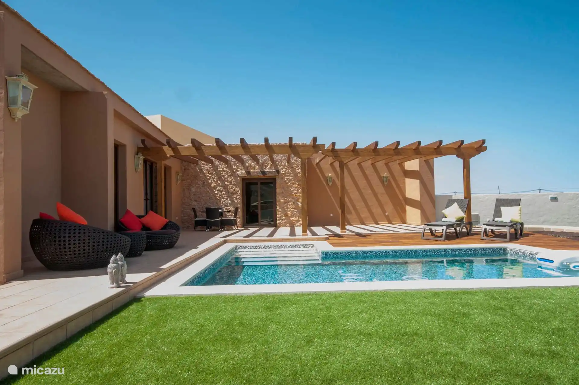 Algemeen uitzicht op de binnenplaats vanaf het gazon, met de zwembadtrap, pergola en ligstoelen in de zon.