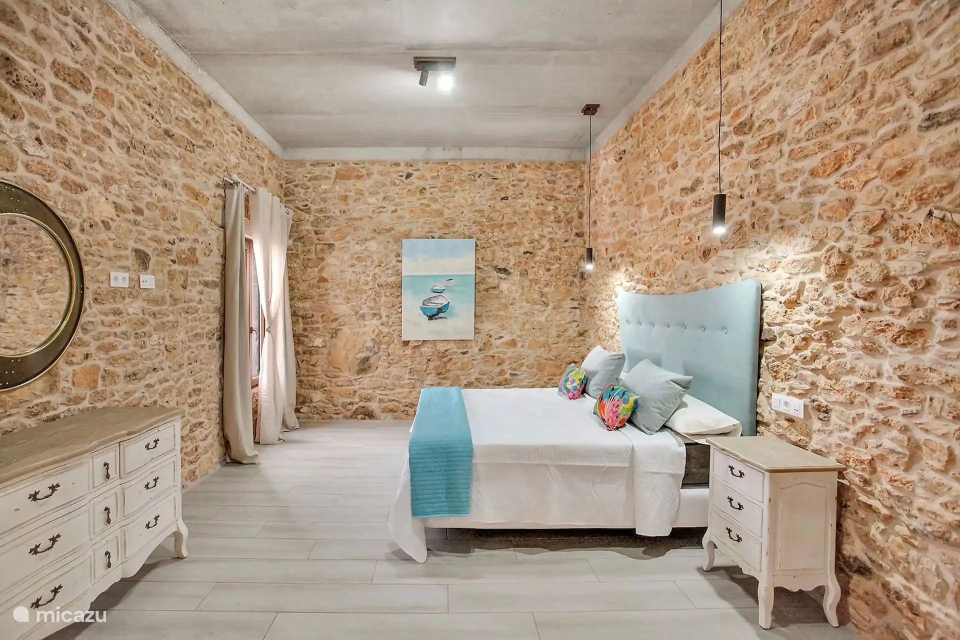 El dormitorio desde el otro extremo, con la cómoda blanca, el espejo redondo y la ventana con cortinas.